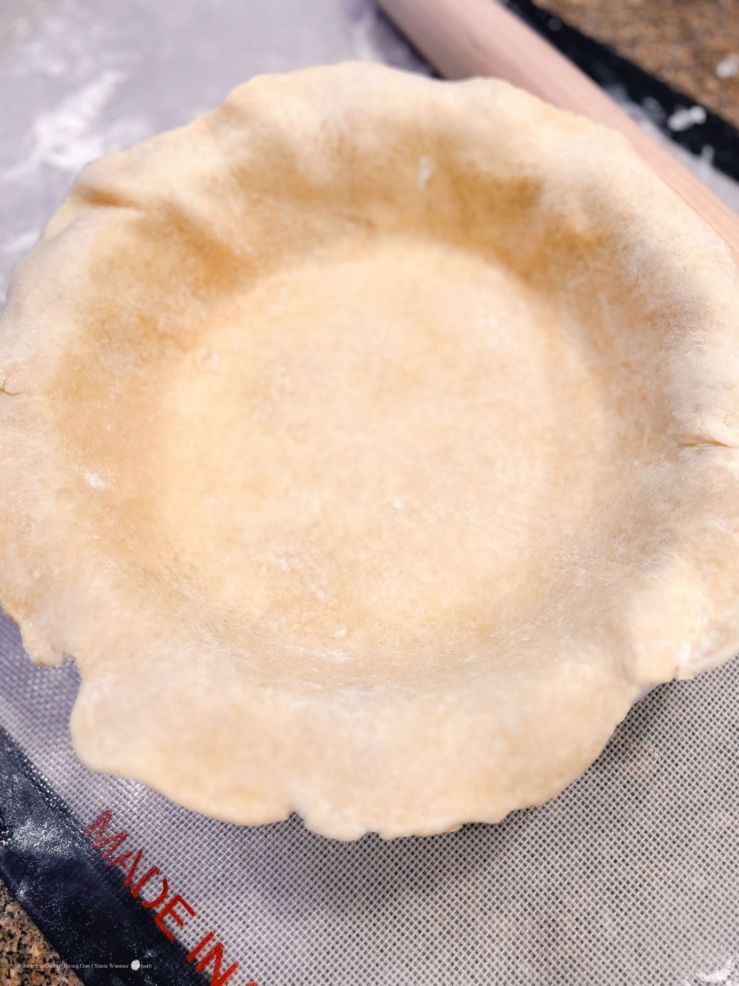 Raw pie dough being shaped into a circular form on a silicone mat.