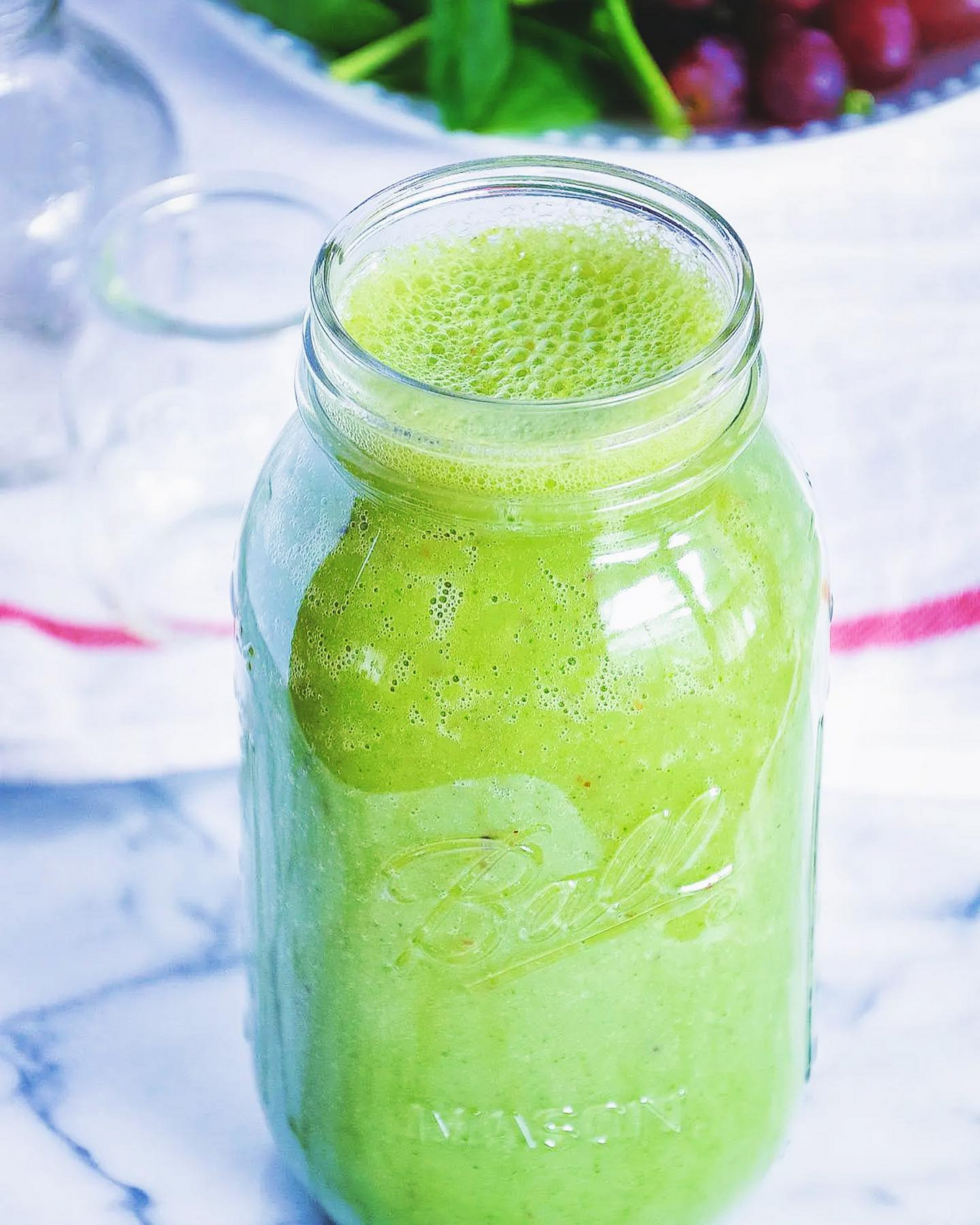 Bright green healthy smoothie in a mason jar with frothy top layer.