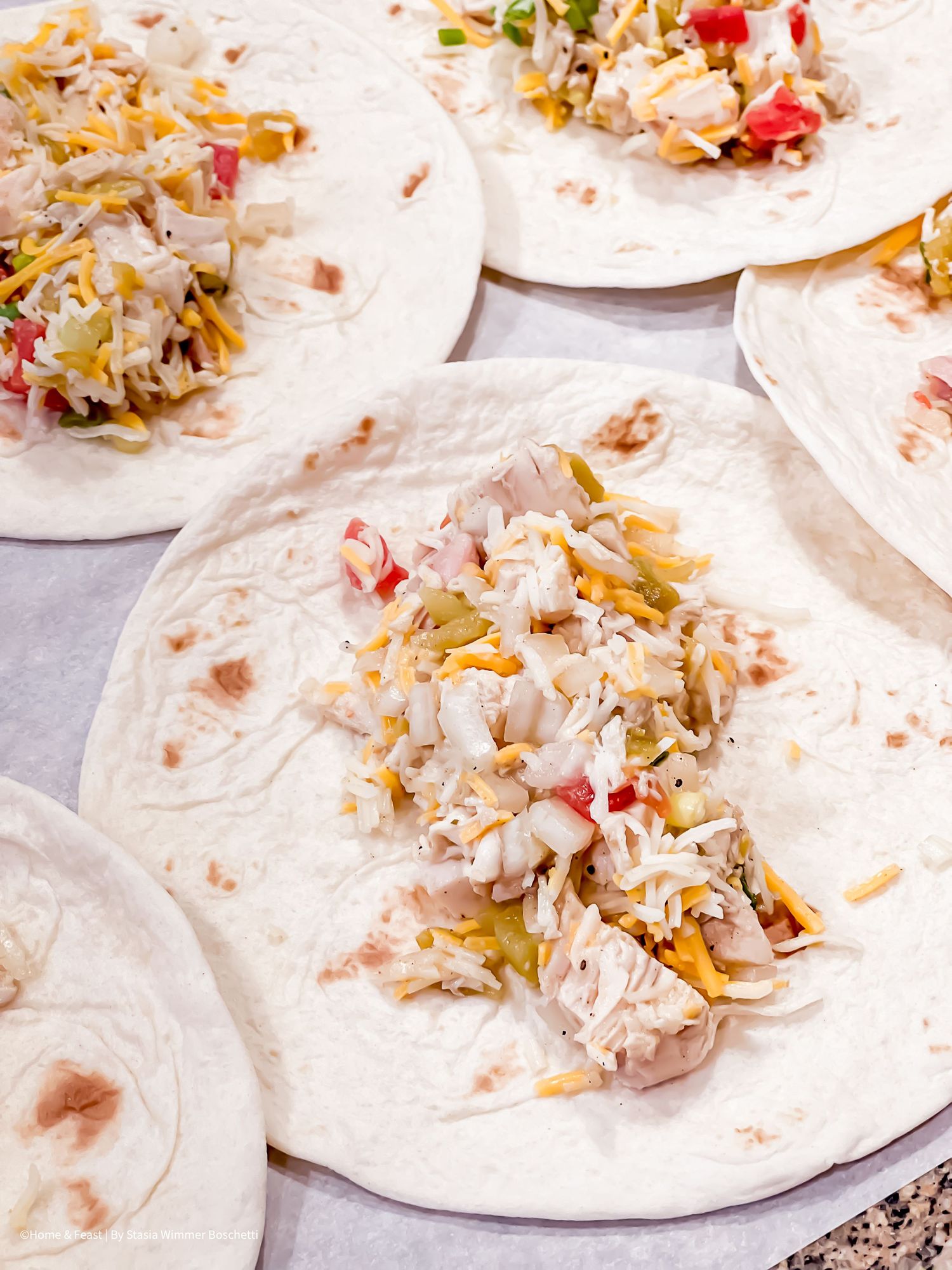 Flour tortillas filled with shredded chicken, cheese and vegetables laid out in preparation.
