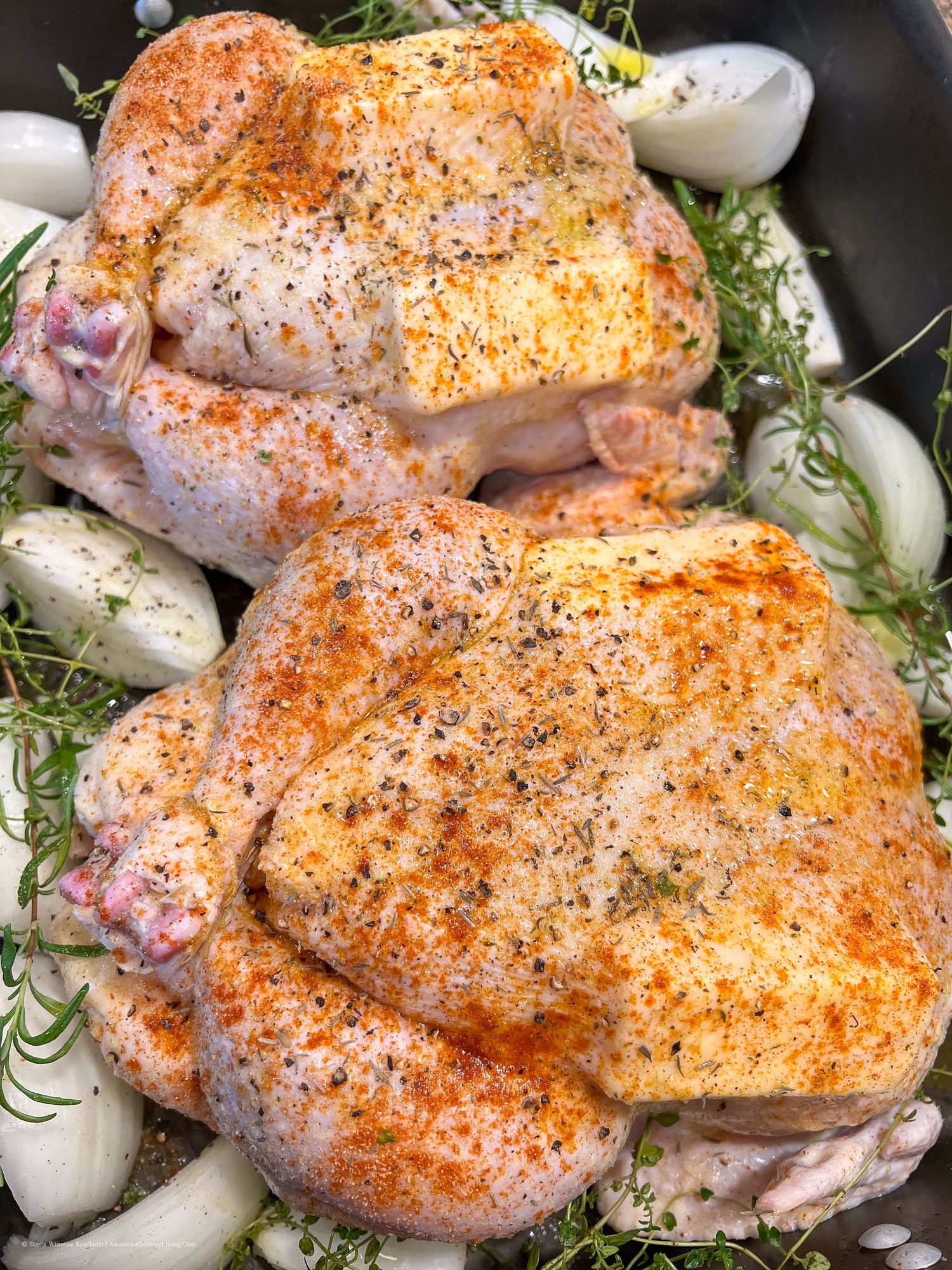 Raw chicken thighs dusted with seasonings and fresh herbs in a black pan.