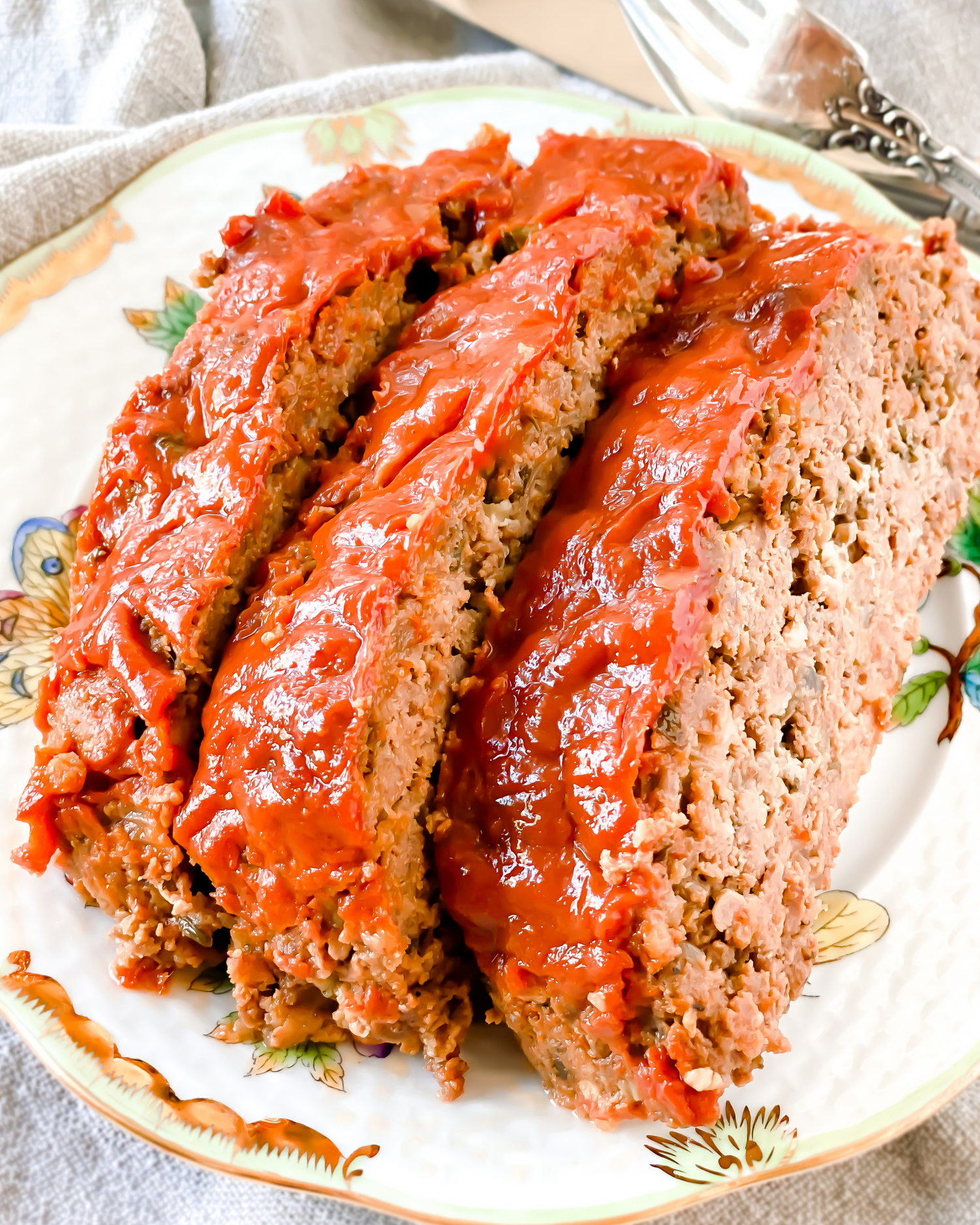 Sliced homemade meatloaf glazed with red sauce served on a decorative plate.