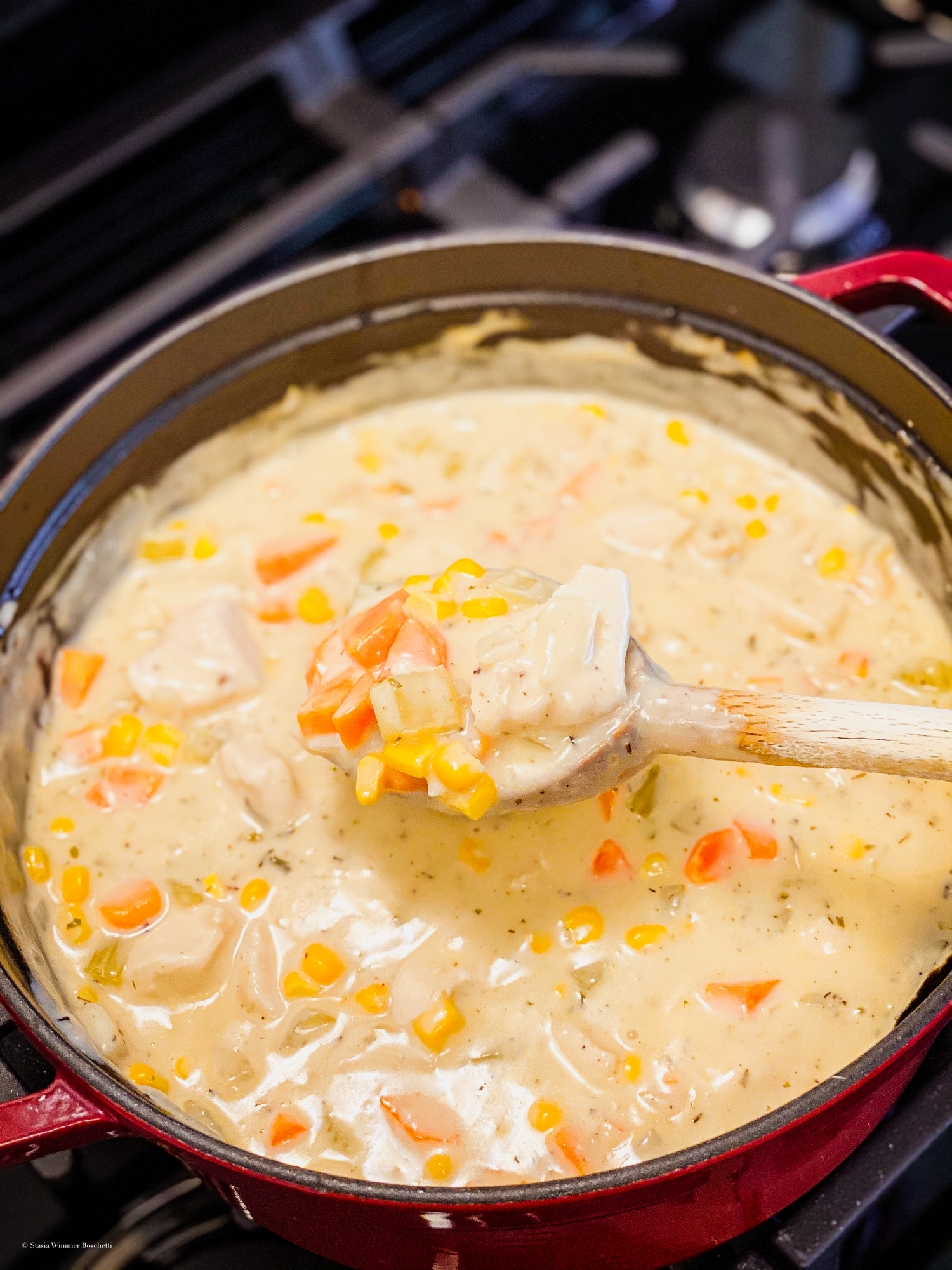 Creamy chicken soup with vegetables simmering in a red Dutch oven.