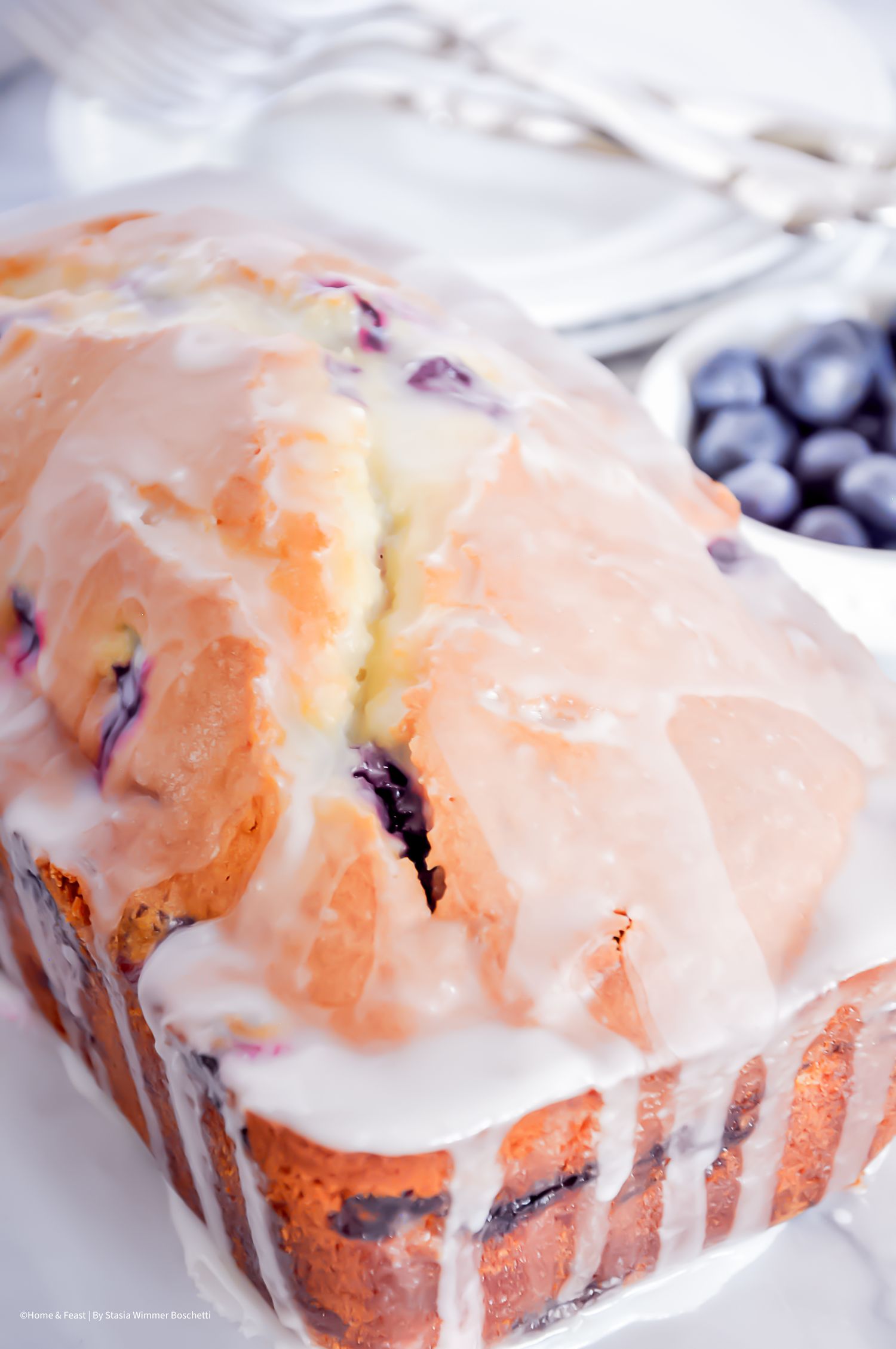 Glazed blueberry muffins with white icing drizzle on a marble countertop.