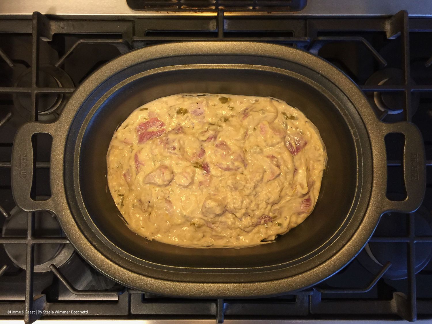 Meat and cream sauce mixture cooking and browning in oval dish.