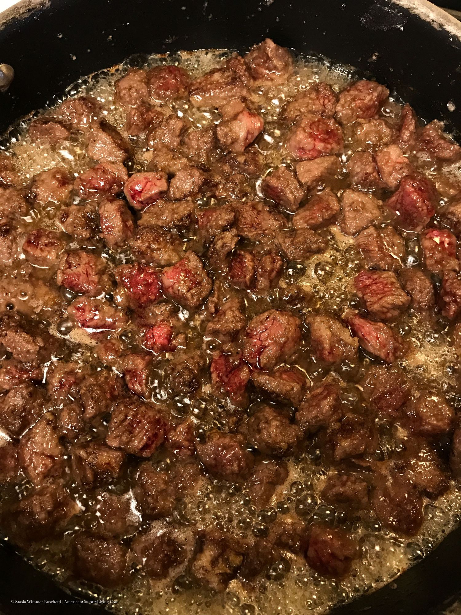 Cubed beef searing in a cast iron skillet with bubbling oil and juices.