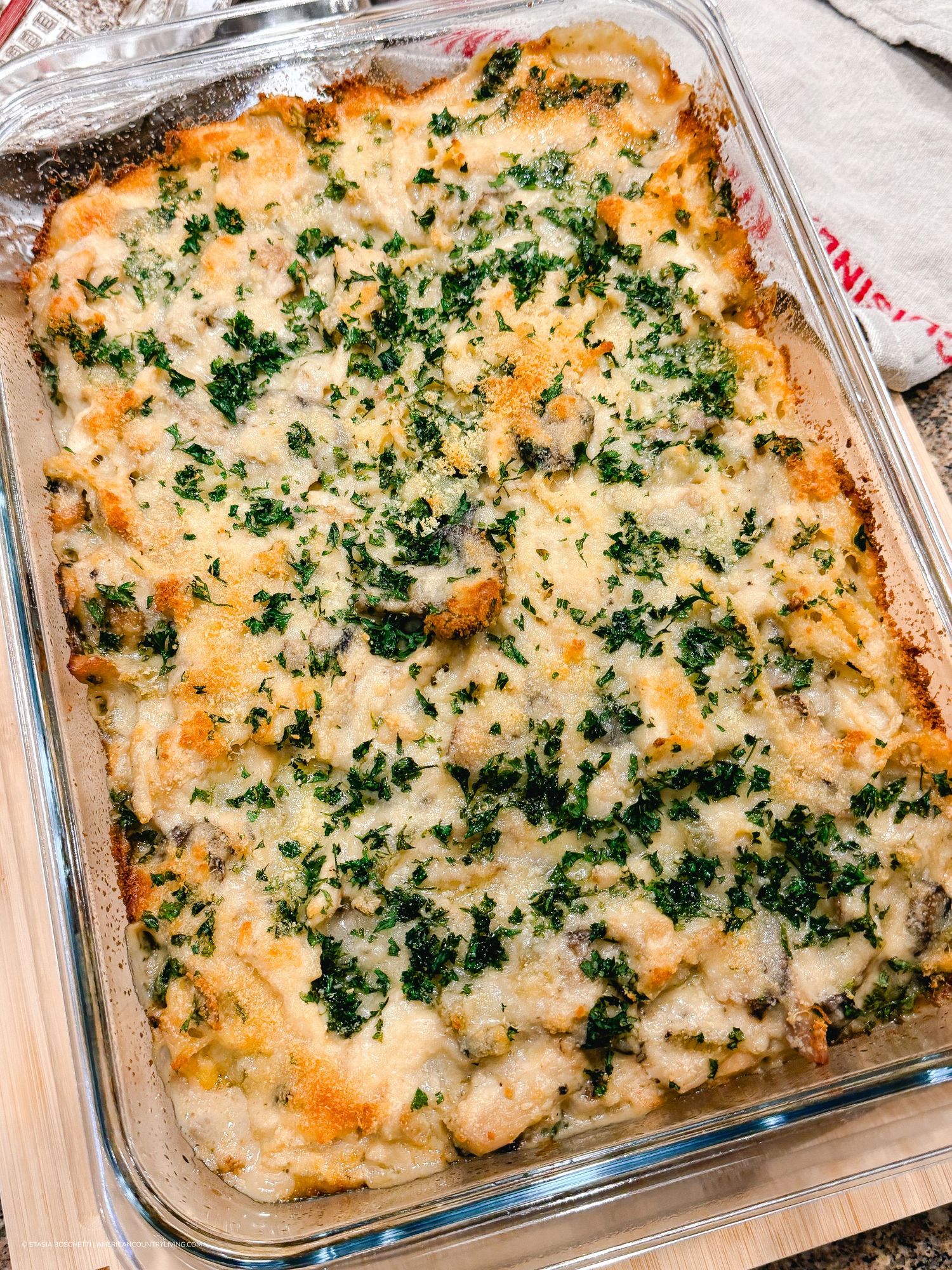 Golden baked casserole dish topped with melted cheese, sautéed mushrooms, and chopped parsley in a glass baking pan.