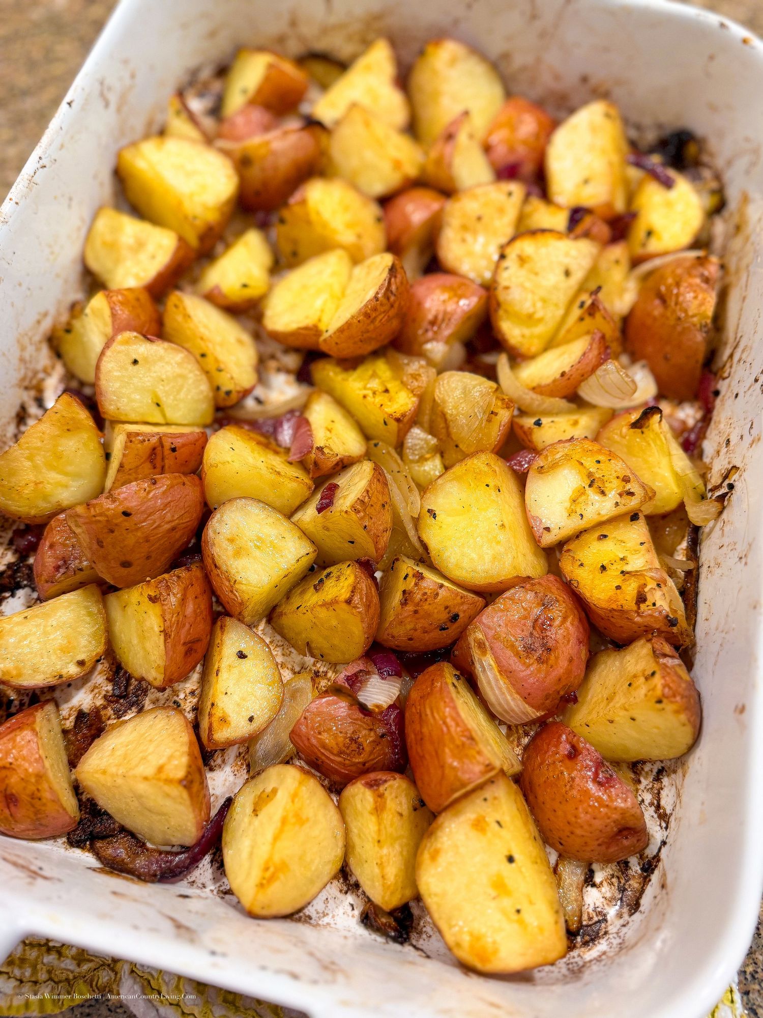 Golden roasted red potatoes seasoned with herbs, baked to perfection in a white ceramic baking dish.