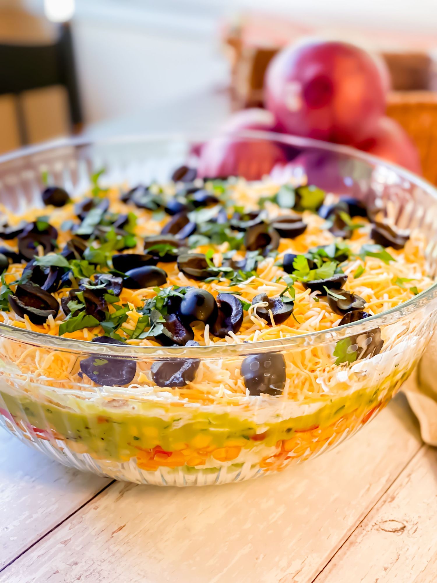 Seven-layer taco dip garnished with black olives and shredded cheese in a clear glass serving dish.