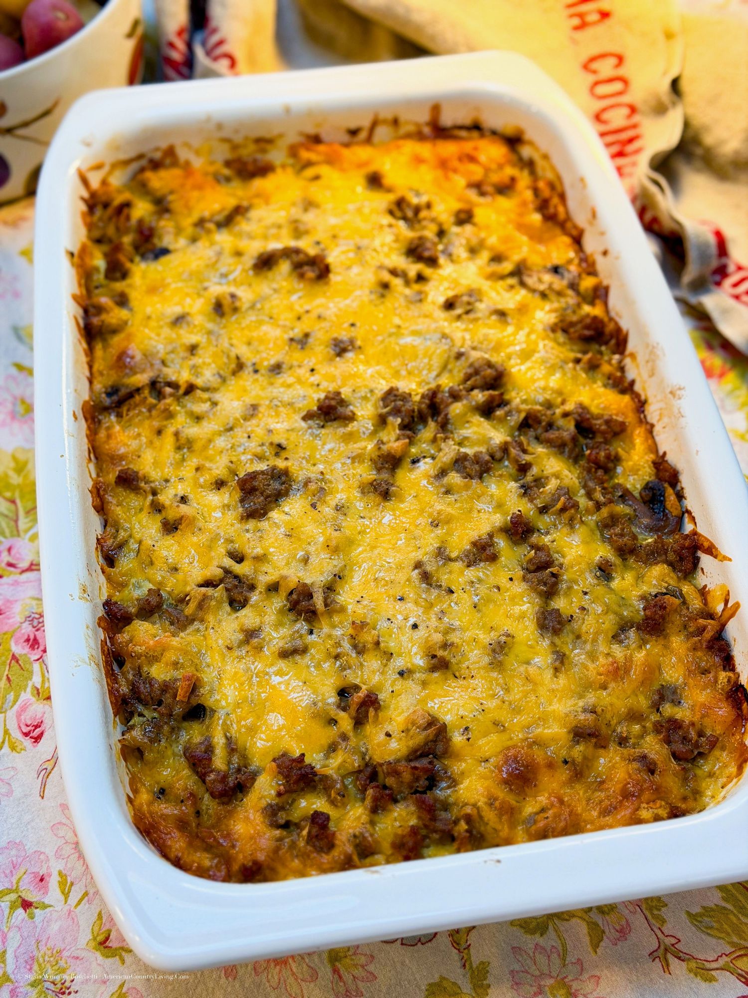 Golden cheesy breakfast casserole with sausage and hash browns baked in a white rectangular dish.