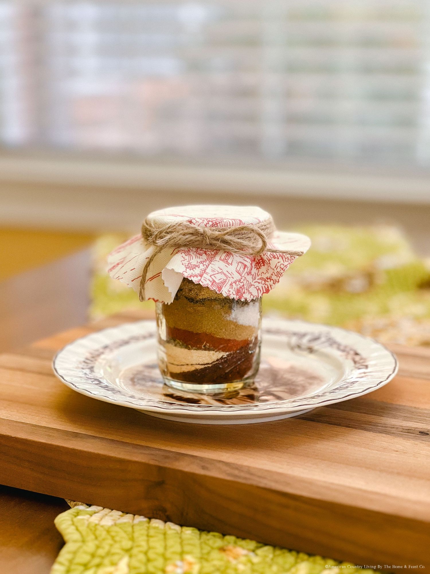 Homemade hot cocoa mix layers in a glass jar with decorative paper topping on wooden surface.