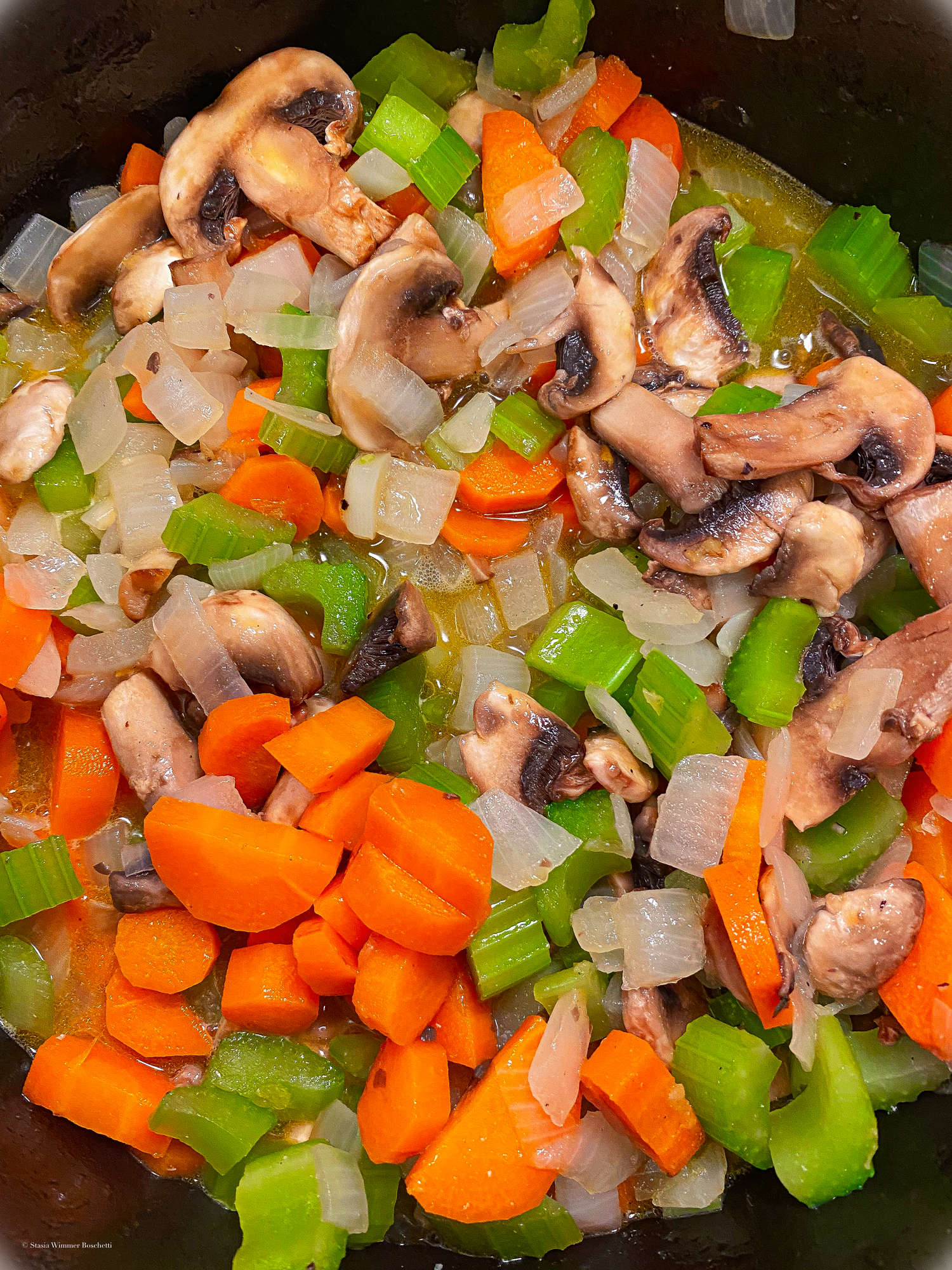 Fresh mushrooms, carrots and celery cooking together in a dark skillet.