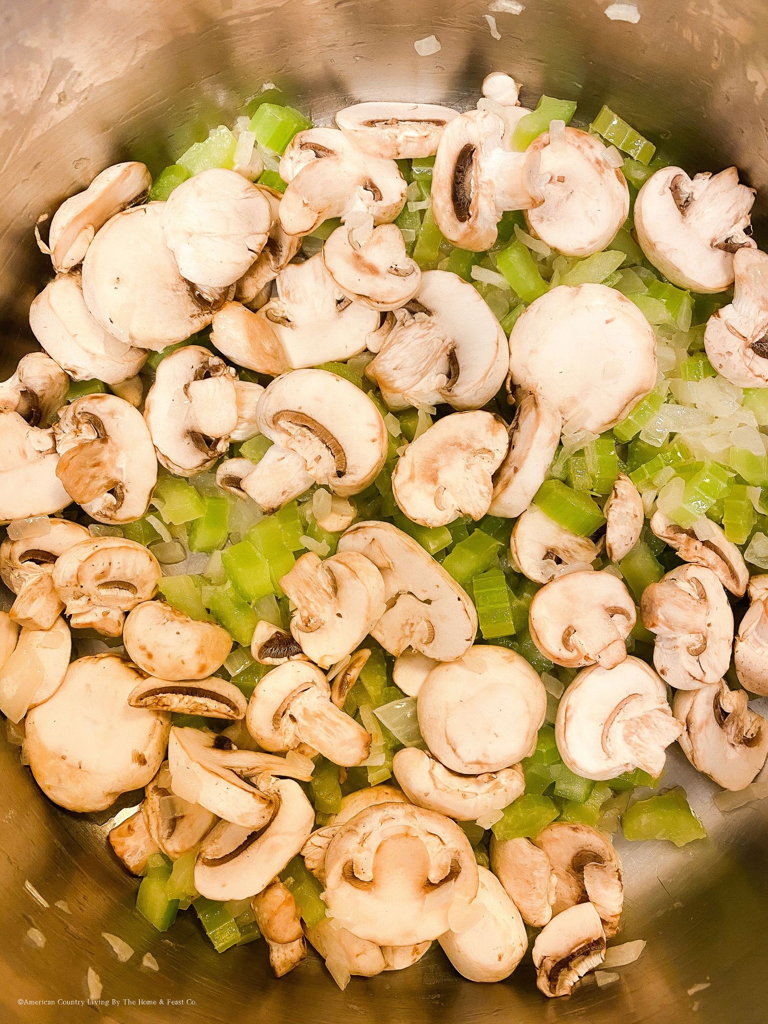Fresh sliced mushrooms and celery sautéing in a stainless steel pan.
