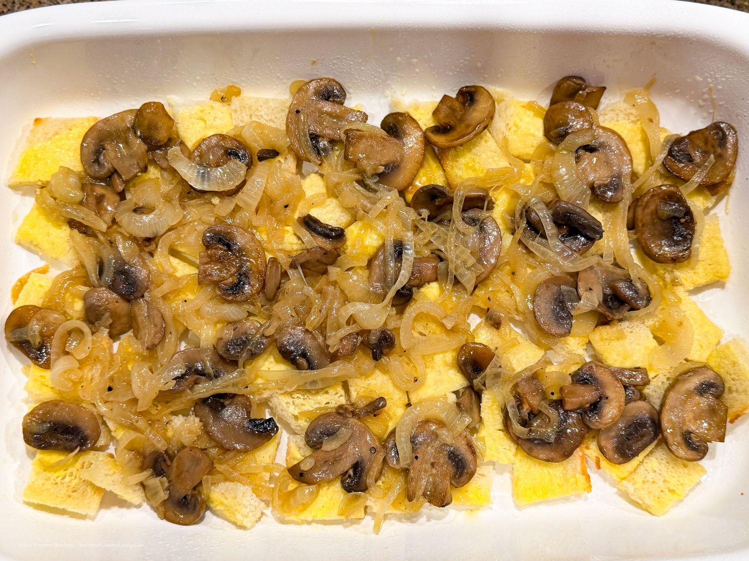 Baked casserole dish with sliced potatoes topped with caramelized onions and sautéed mushrooms.