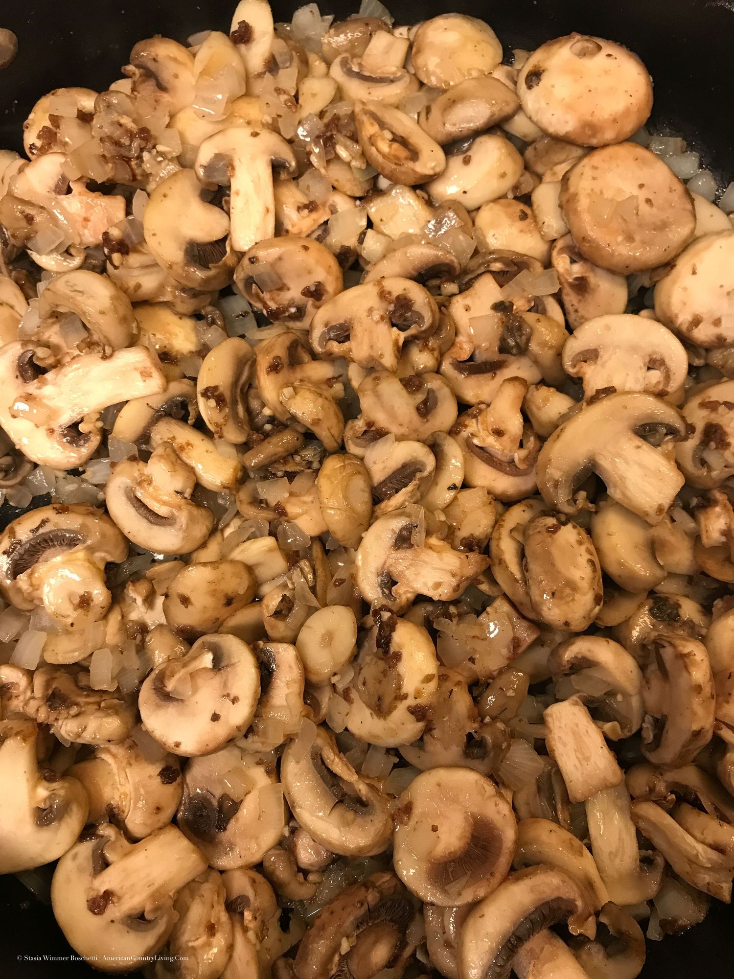 Sliced mushrooms sauteing with onions in a cast iron skillet until golden brown.