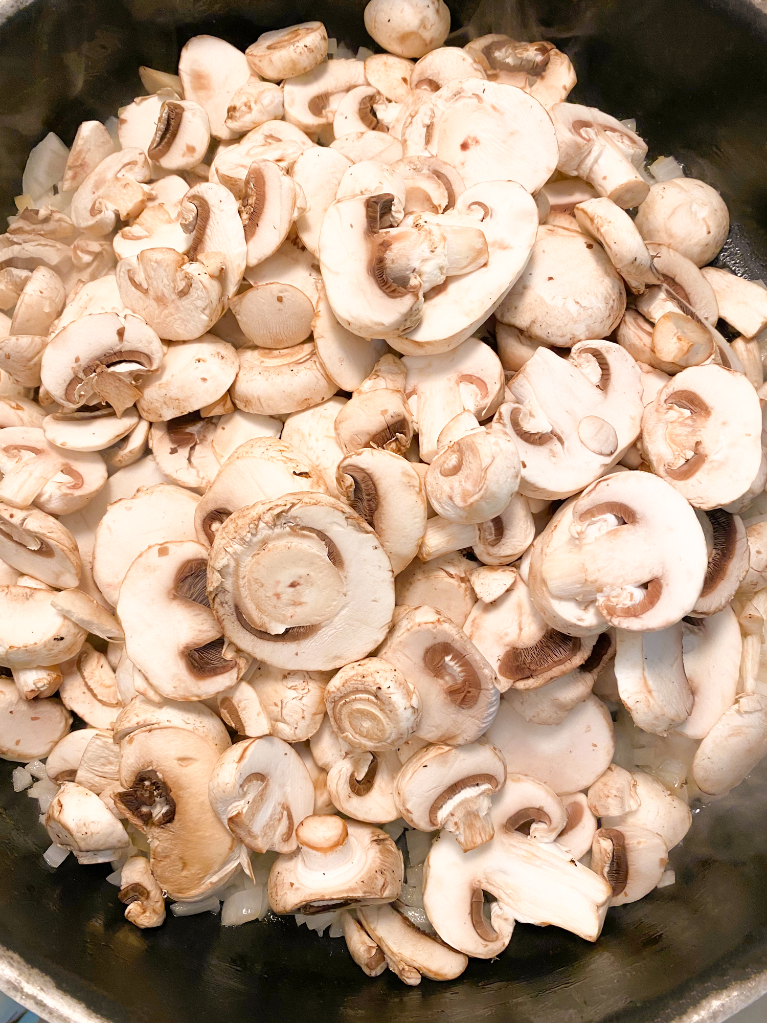 Fresh sliced white mushrooms cooking in a black pan.