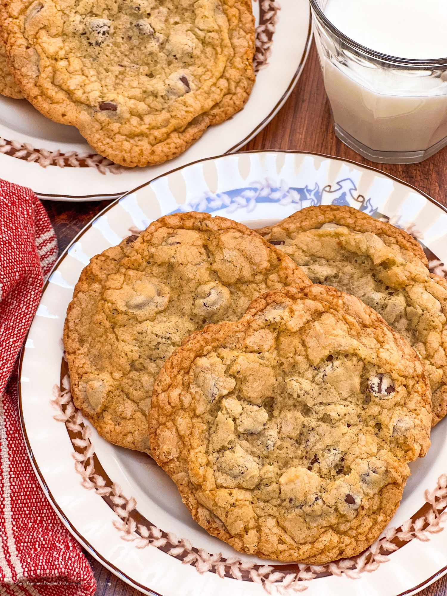 Golden chocolate chip cookies arranged on decorative plates with glasses of milk.