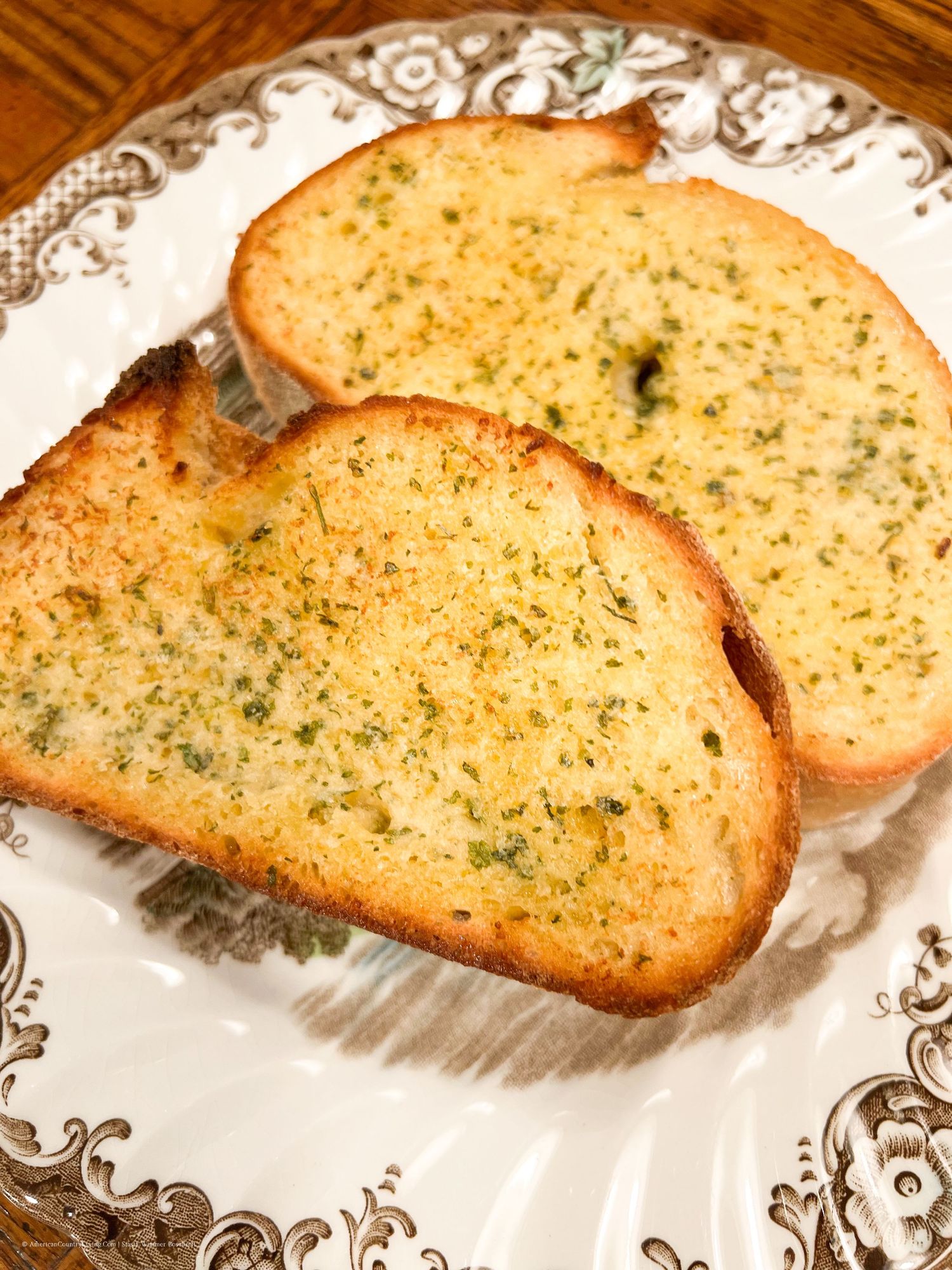 Crusty garlic bread pieces displayed on vintage-style plates with ornate designs.