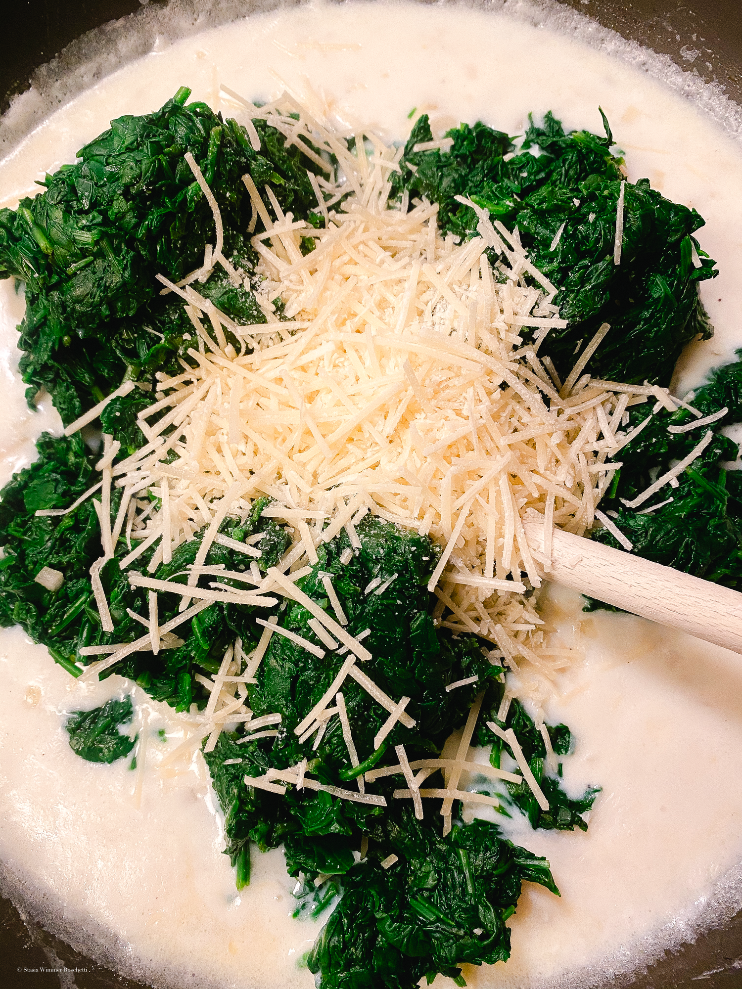 Fresh chopped spinach and shredded cheese being combined on a white surface.