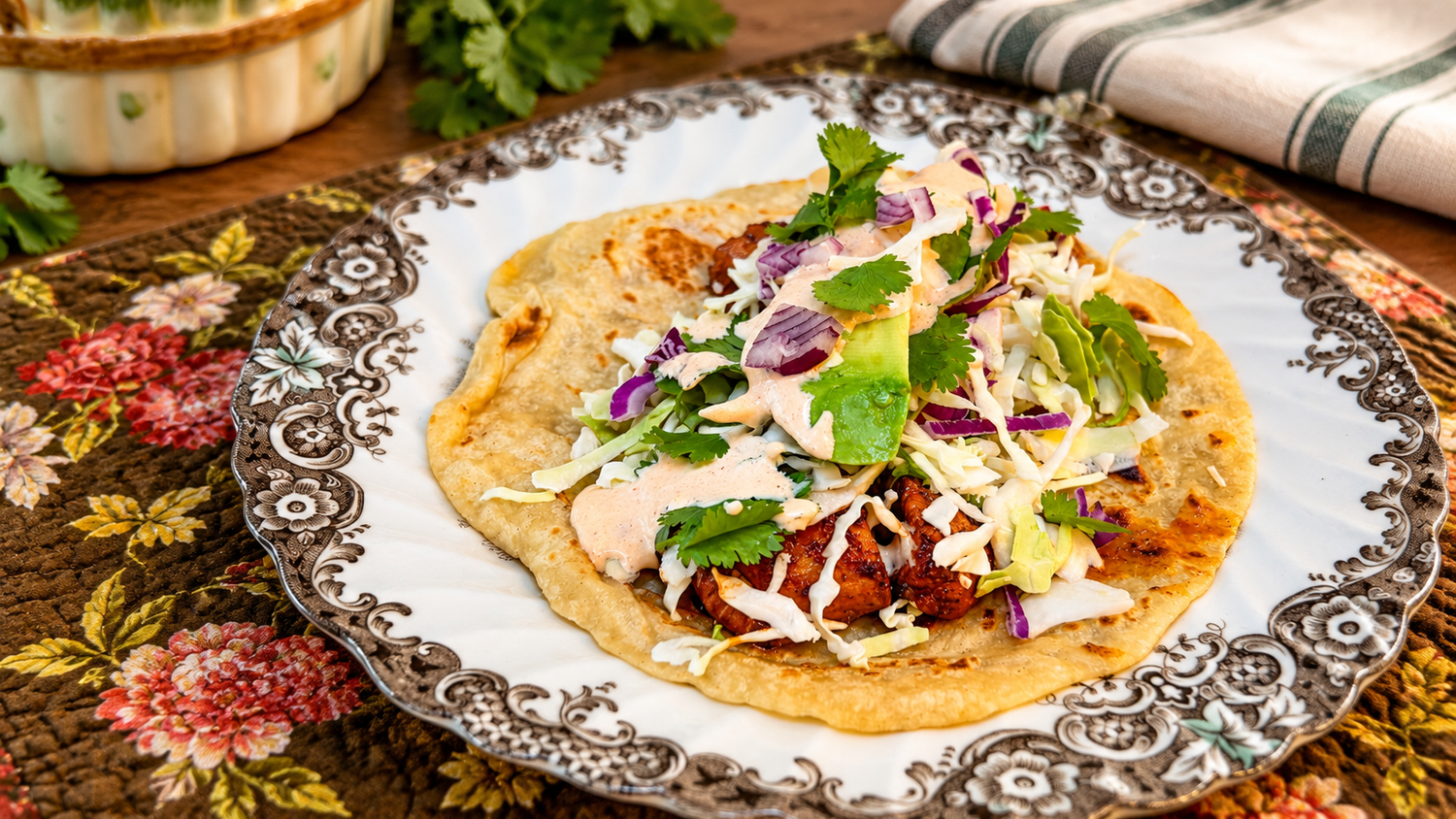 Flatbread taco topped with shredded purple cabbage, fresh cilantro, creamy sauce and seasoned meat on a vintage floral rimmed plate.