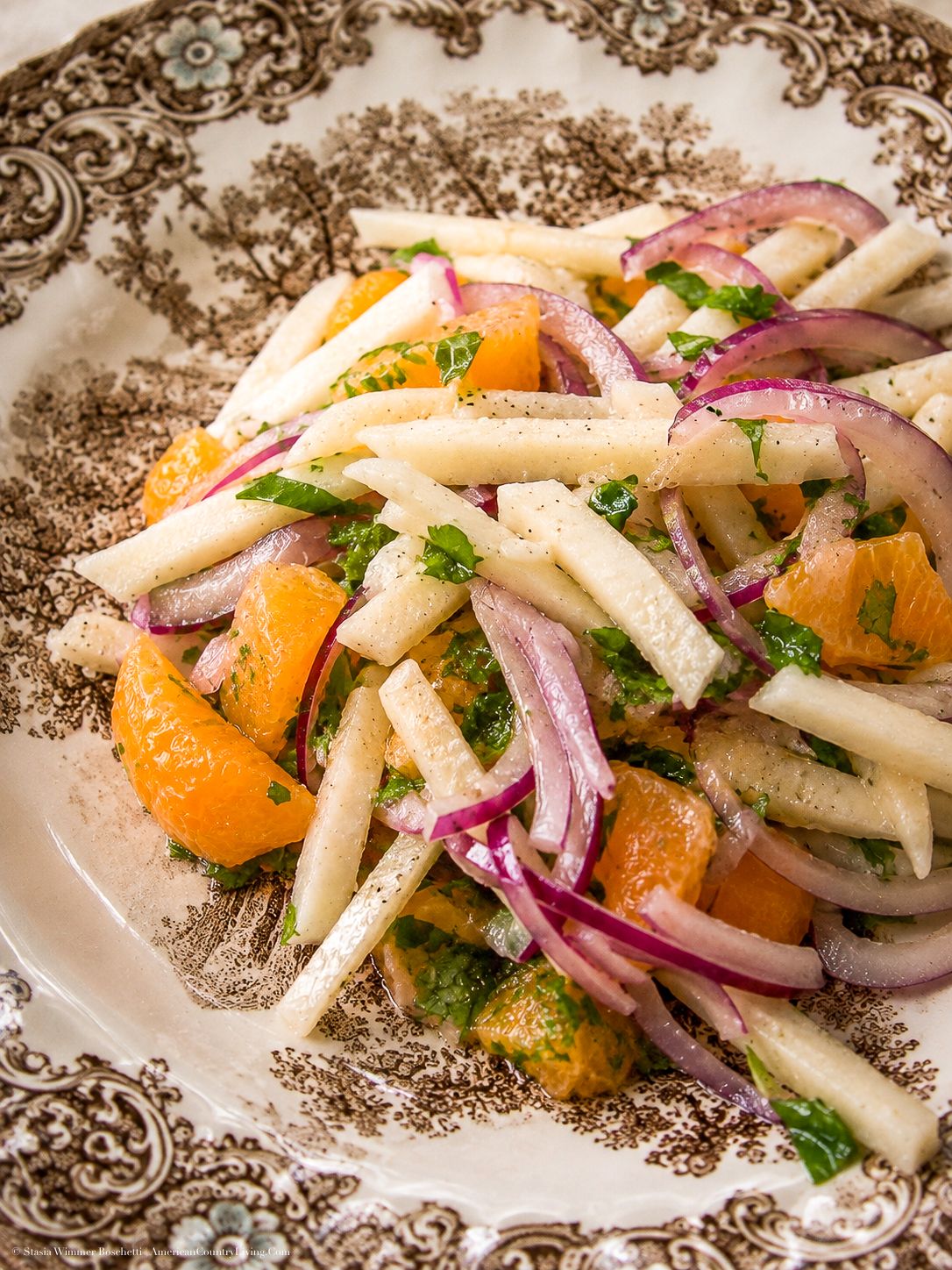 Fresh jicama and orange salad with red onion, herbs, and citrus dressing served on a decorative brown plate.