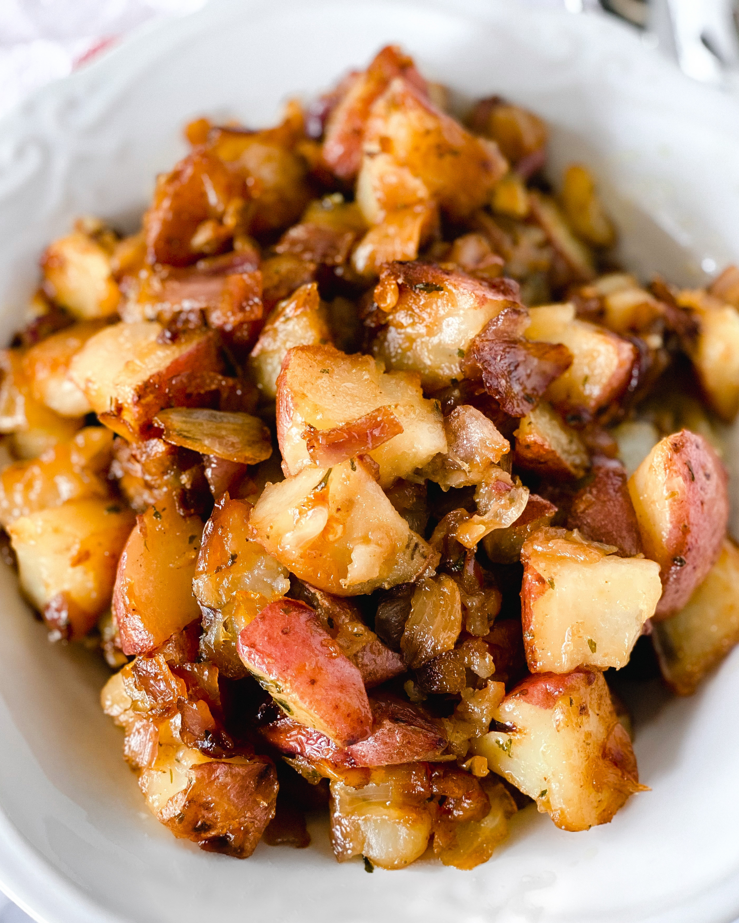 Crispy home fried potatoes with onions and seasonings in a white bowl.