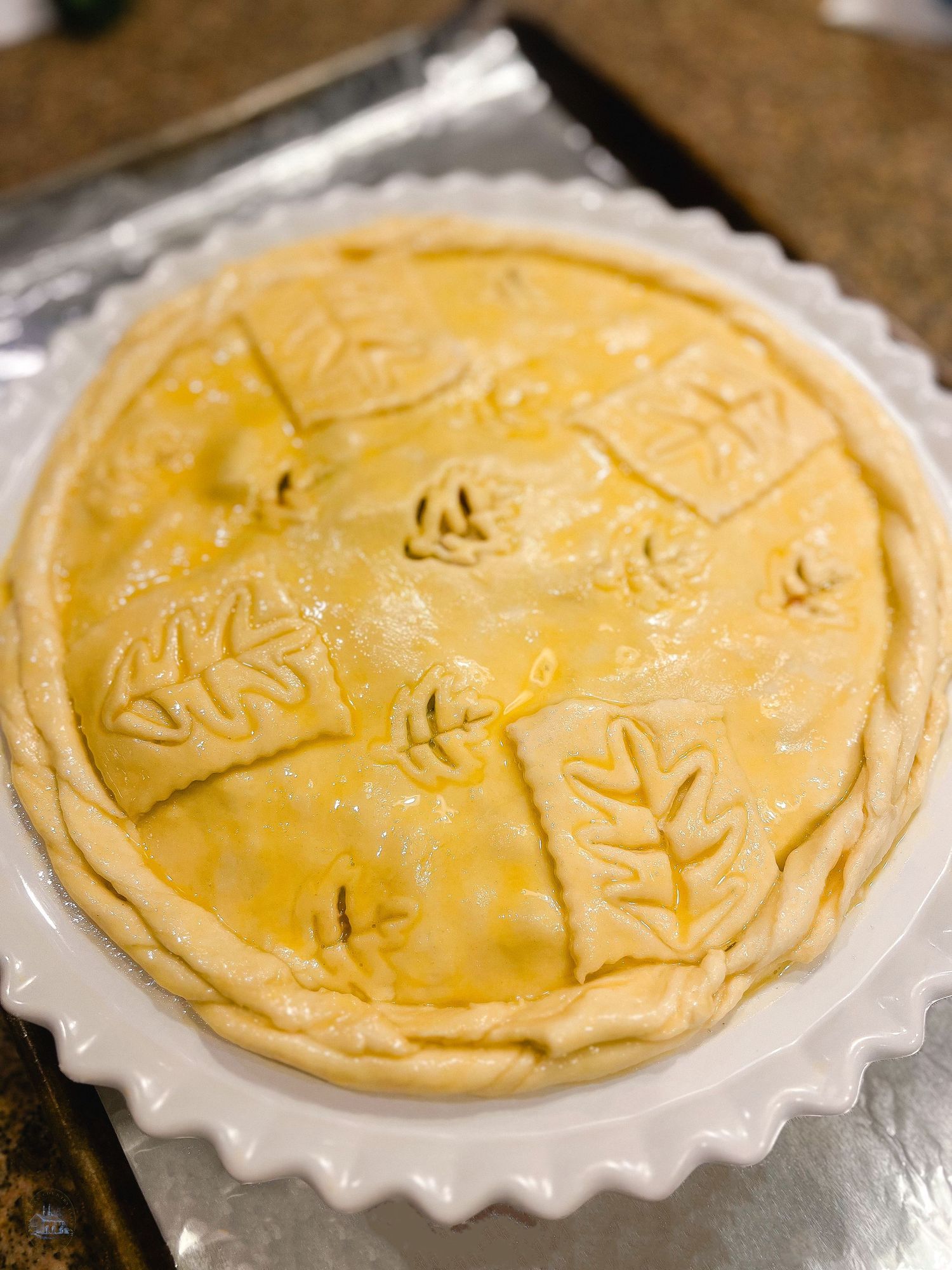Unbaked pie with decorative leaf patterns in pastry crust.
