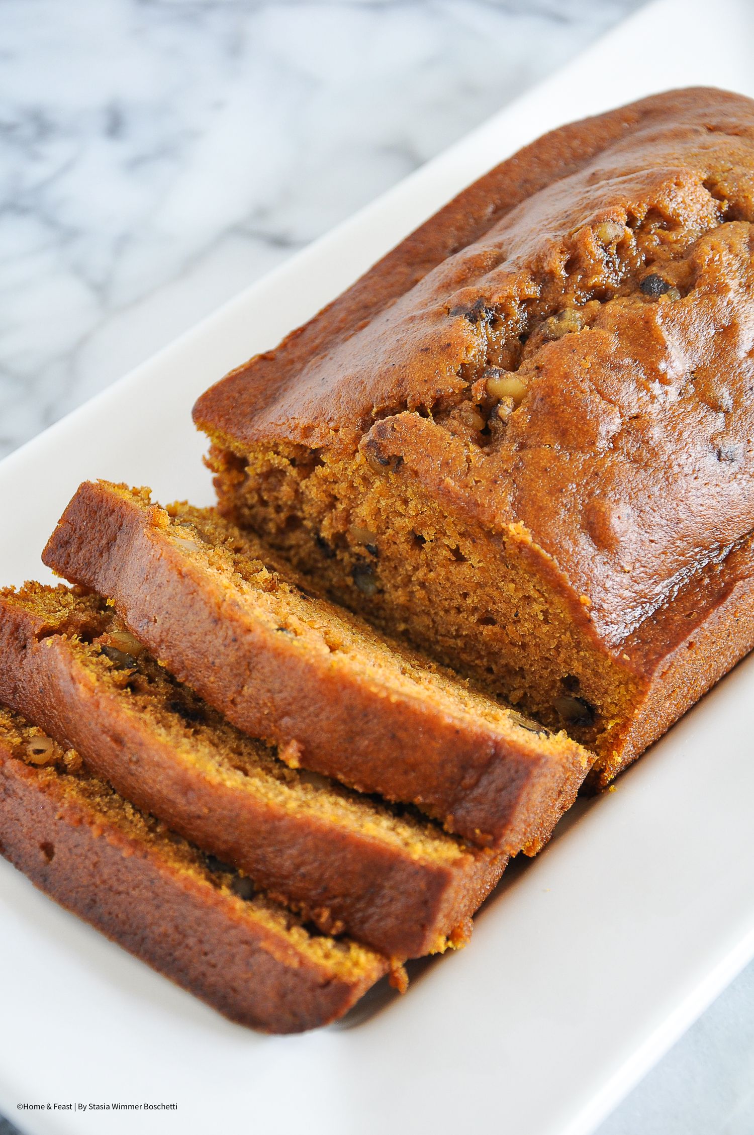 Homemade pumpkin bread loaf sliced to show its moist interior on a white serving plate.