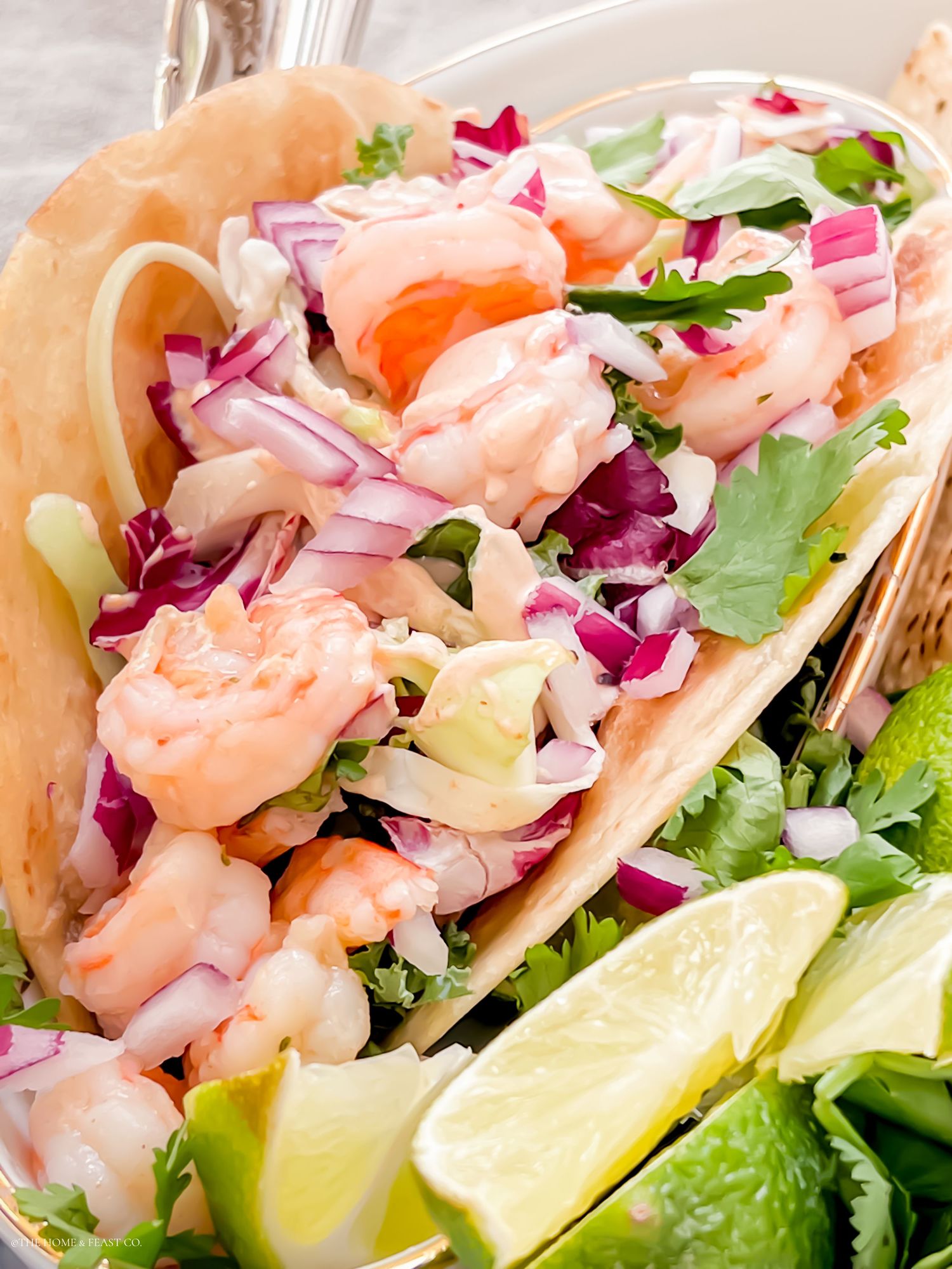 Close up of shrimp taco filled with red cabbage slaw and garnished with fresh lime and herbs.