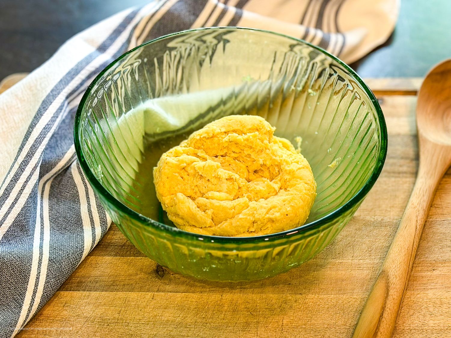 Golden cornbread biscuit served in a vintage green glass ribbed bowl on a wooden cutting board.