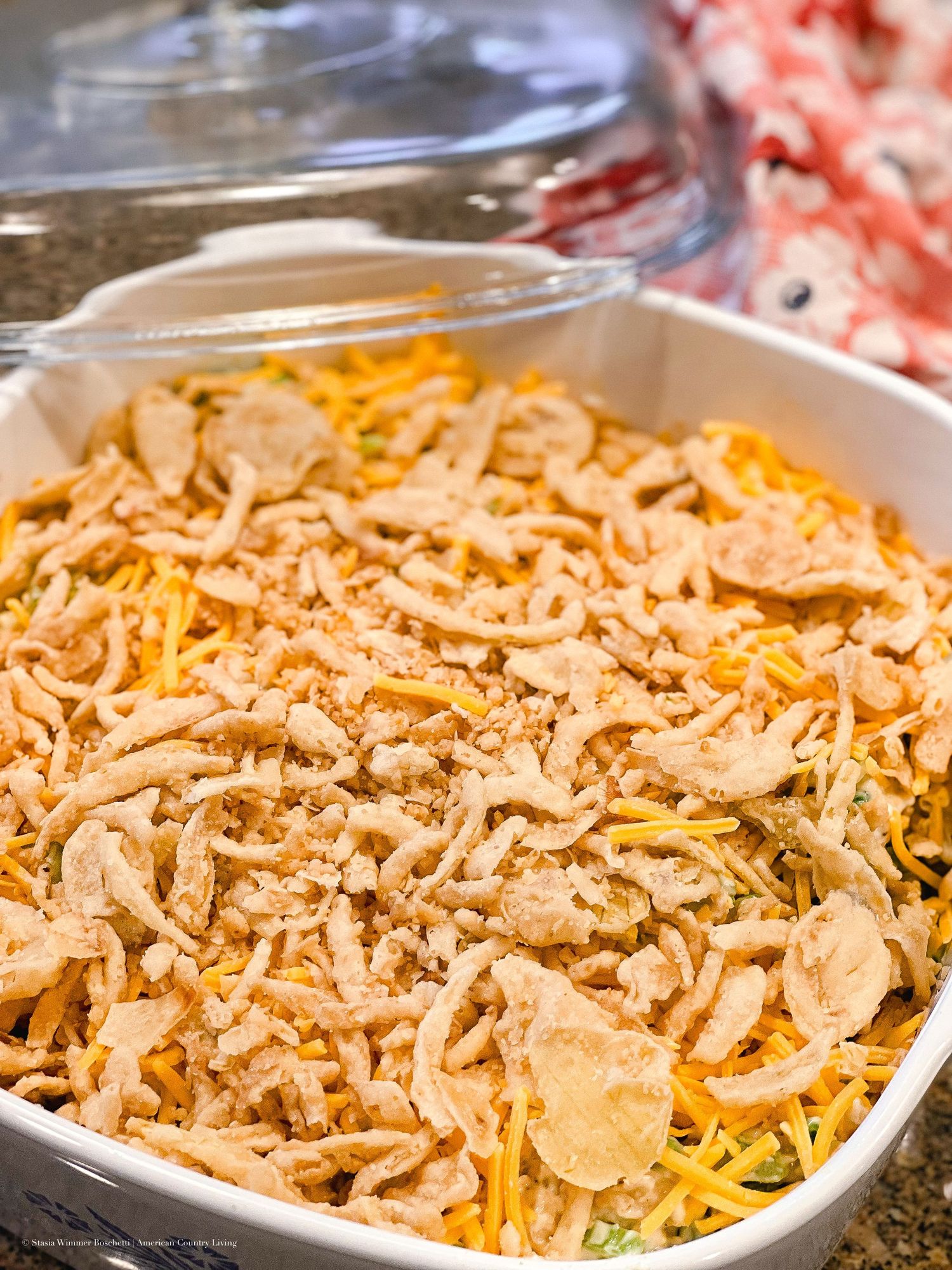 Unbaked casserole with shredded cheese and crispy fried onion topping in white square baking dish.