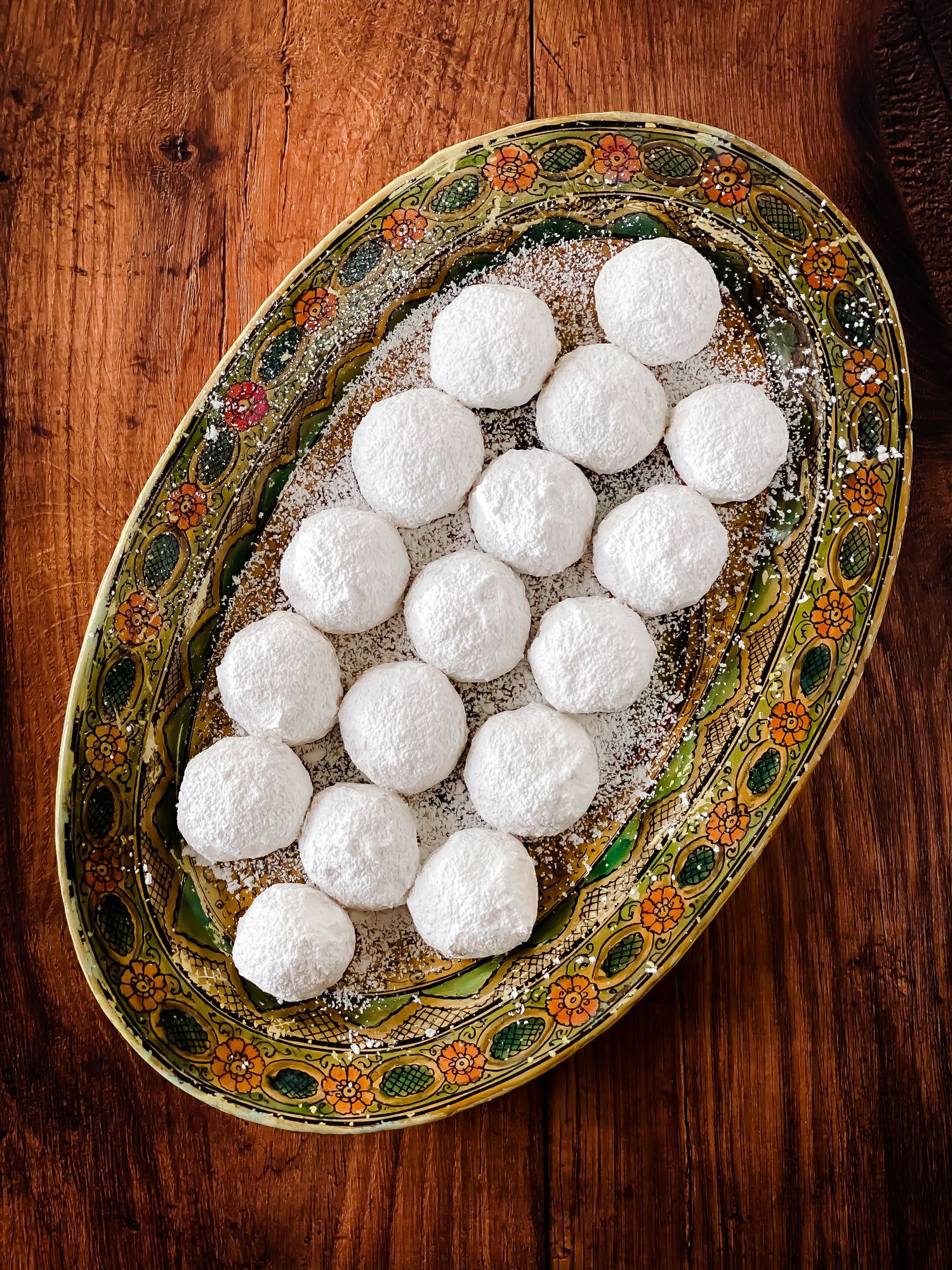 White powdered snowball cookies arranged on an ornate vintage platter with green and gold details.