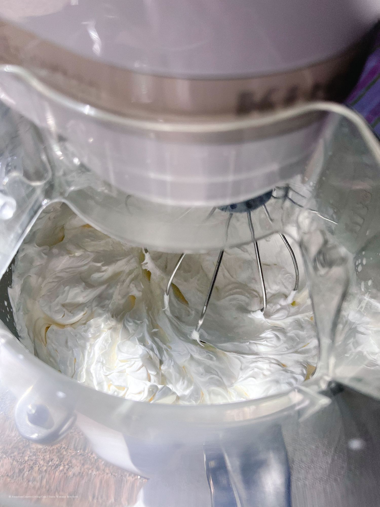 Stand mixer whipping white cream mixture with wire whisk attachment.