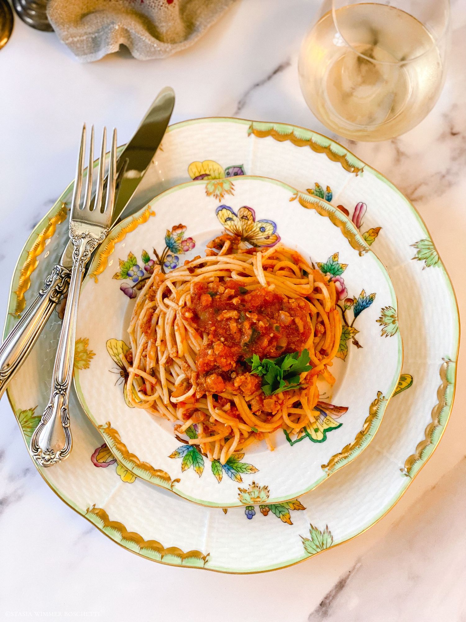 Multiple plates of pasta with red sauce arranged on a white tablecloth with elegant place settings.