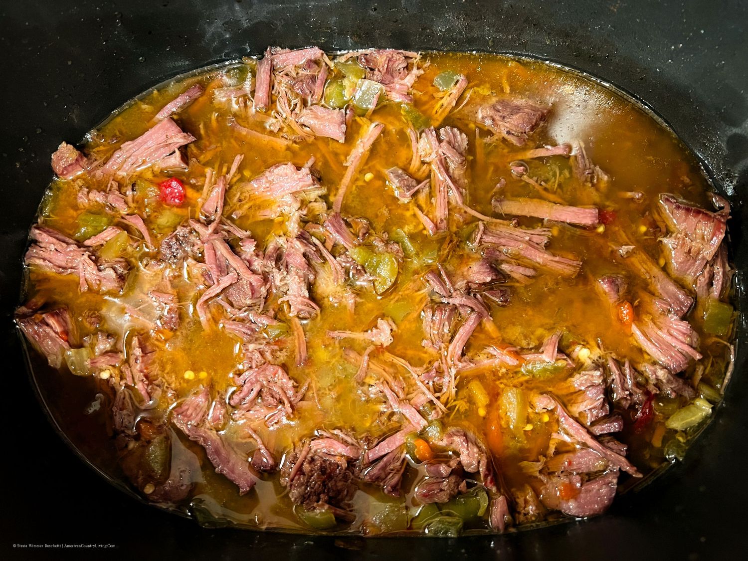 Shredded beef simmering in pan with giardiniera sauce and vegetables.