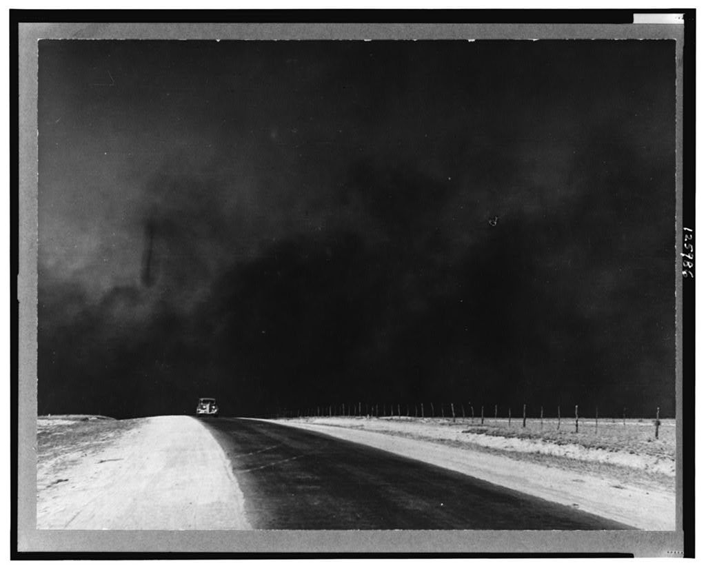 A dark dust storm looms over an empty rural road during the Dust Bowl era of the 1930s.