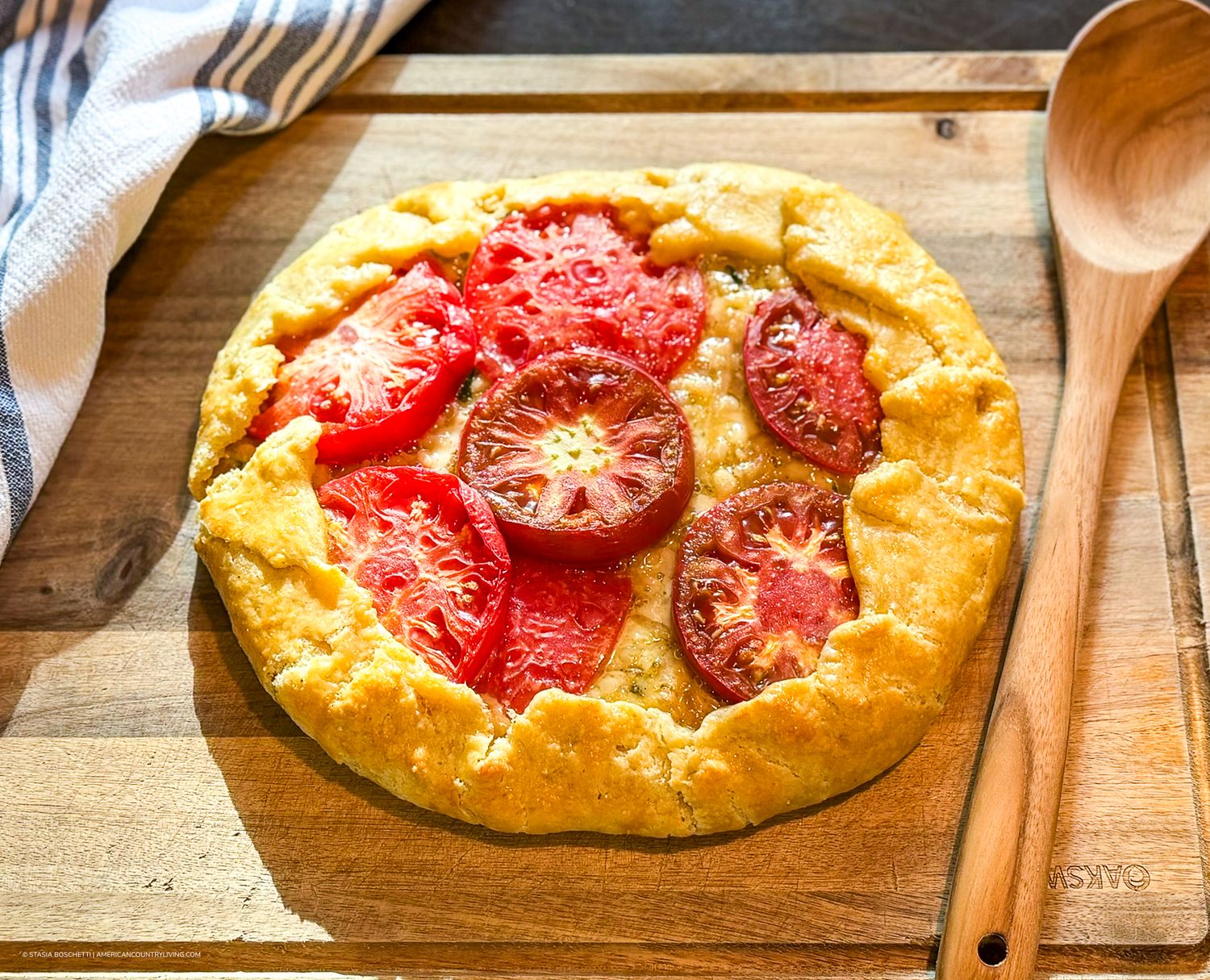 Rustic tomato galette with sliced heirloom tomatoes on golden pastry crust, served on a wooden cutting board.