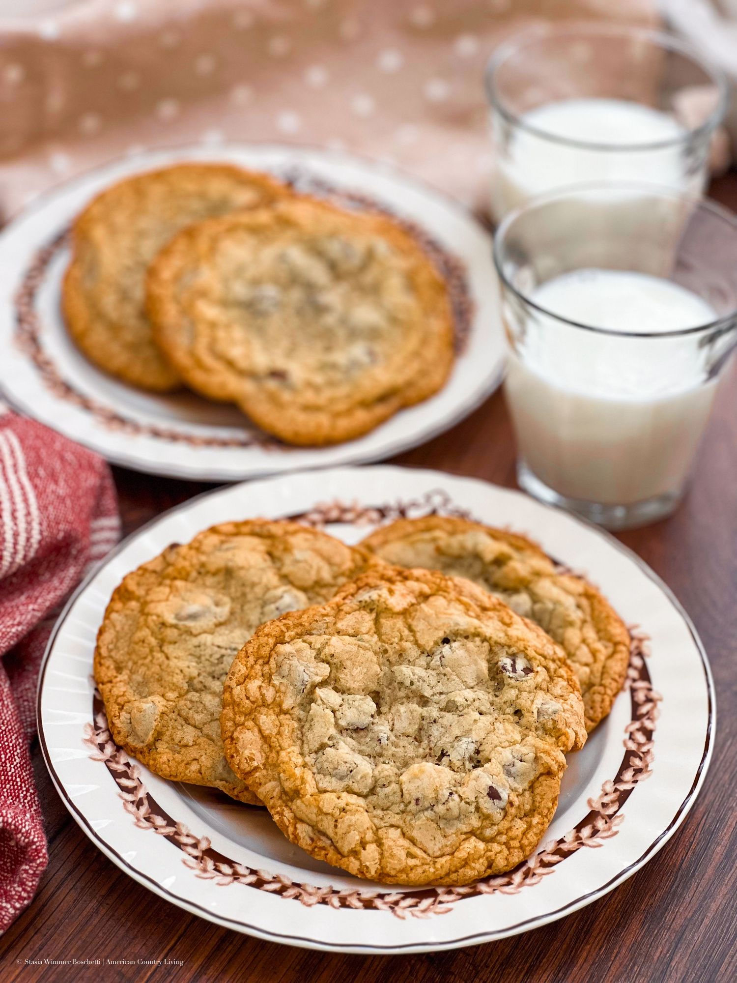 Freshly baked chocolate chip cookies with crispy edges and soft centers served on decorative plates with glasses of milk.