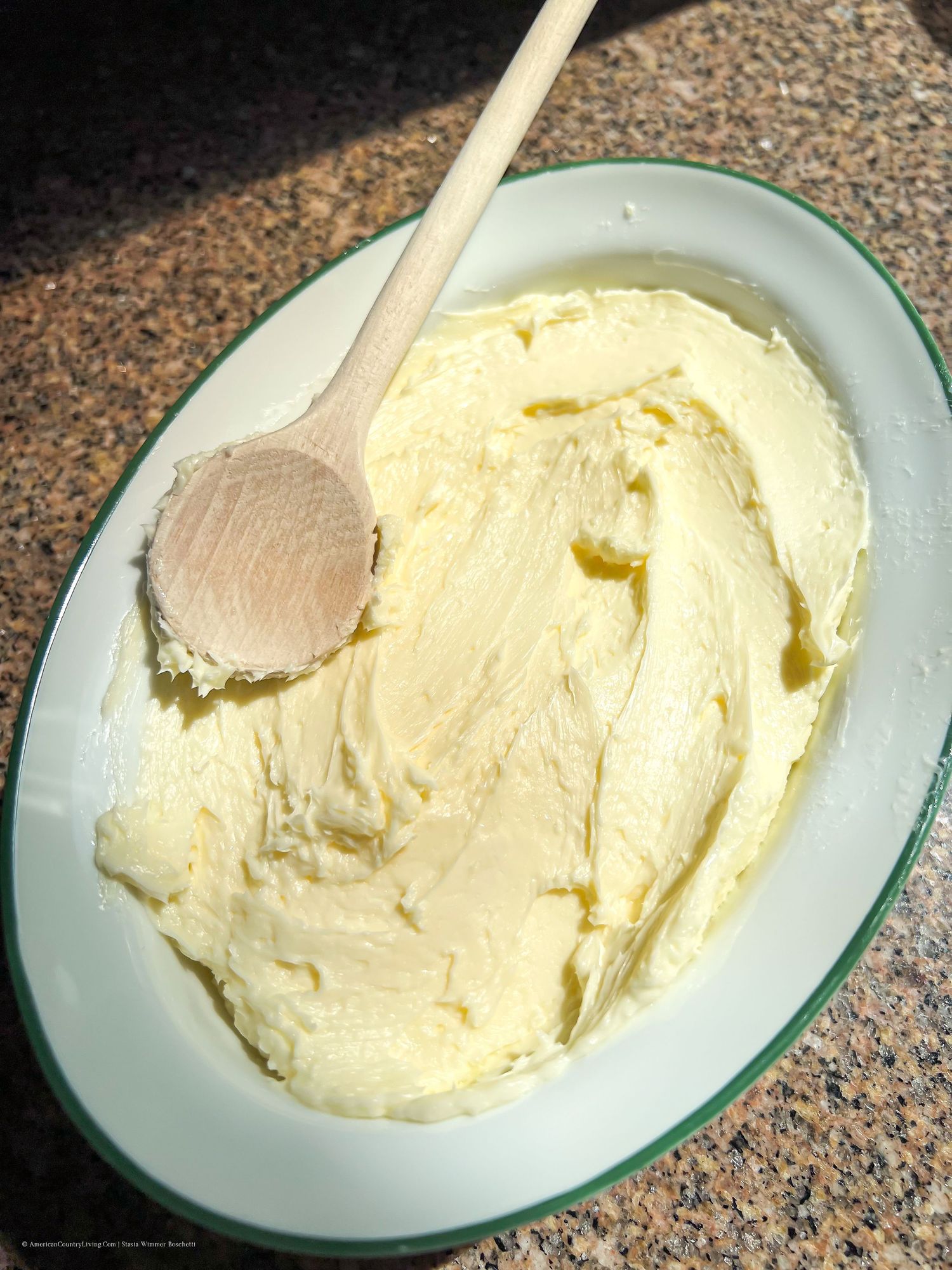 Creamy whipped butter being spread on a white plate with a wooden spoon.