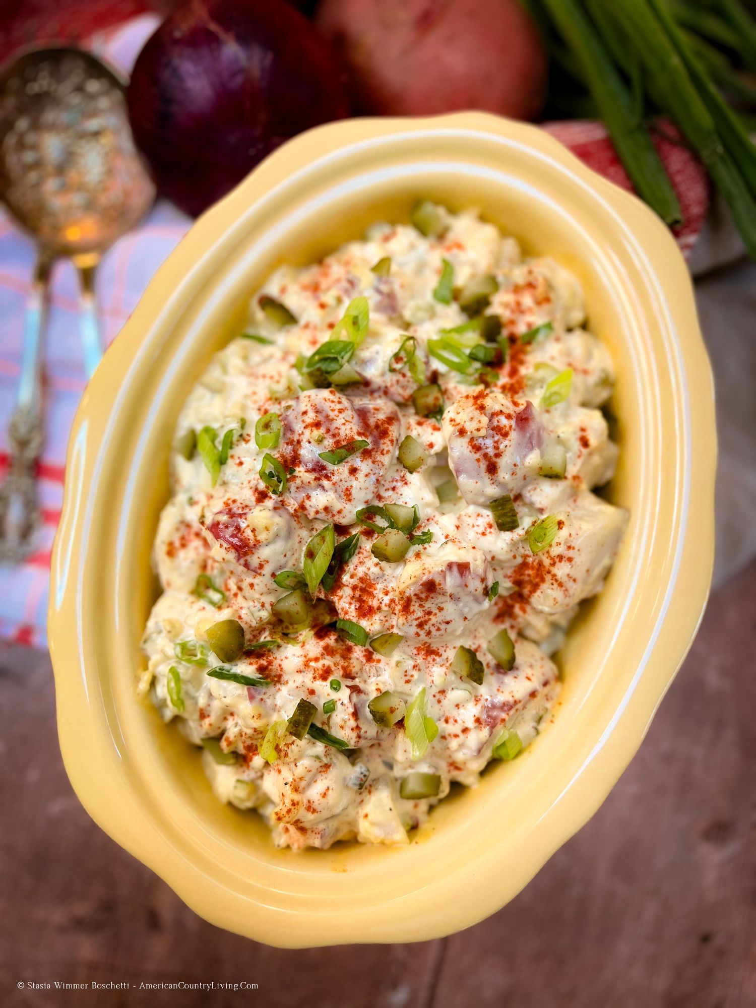 Creamy potato salad garnished with paprika and herbs served in a yellow ceramic bowl.