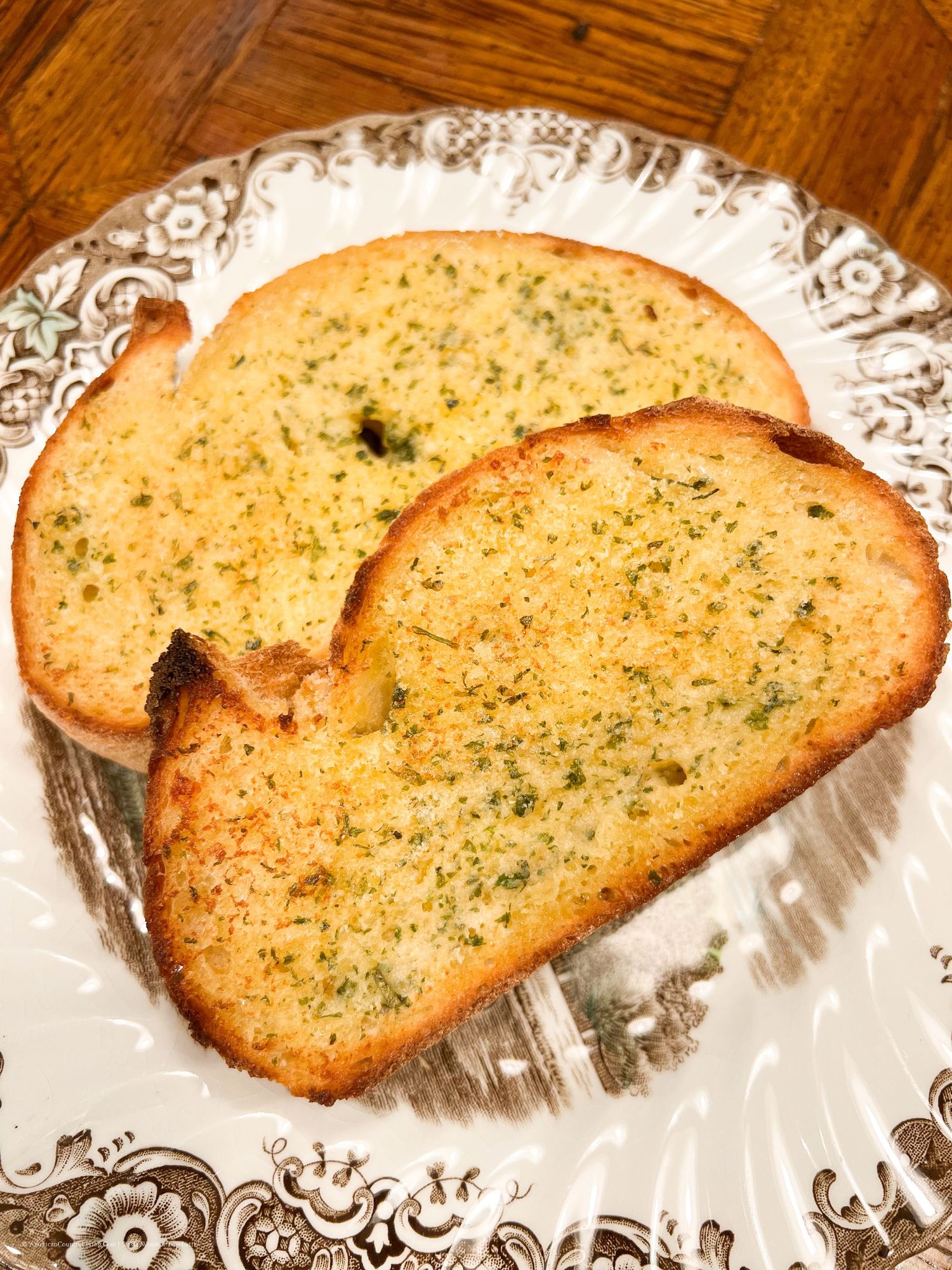 Row of golden-brown toasted garlic bread slices on a decorative plate.