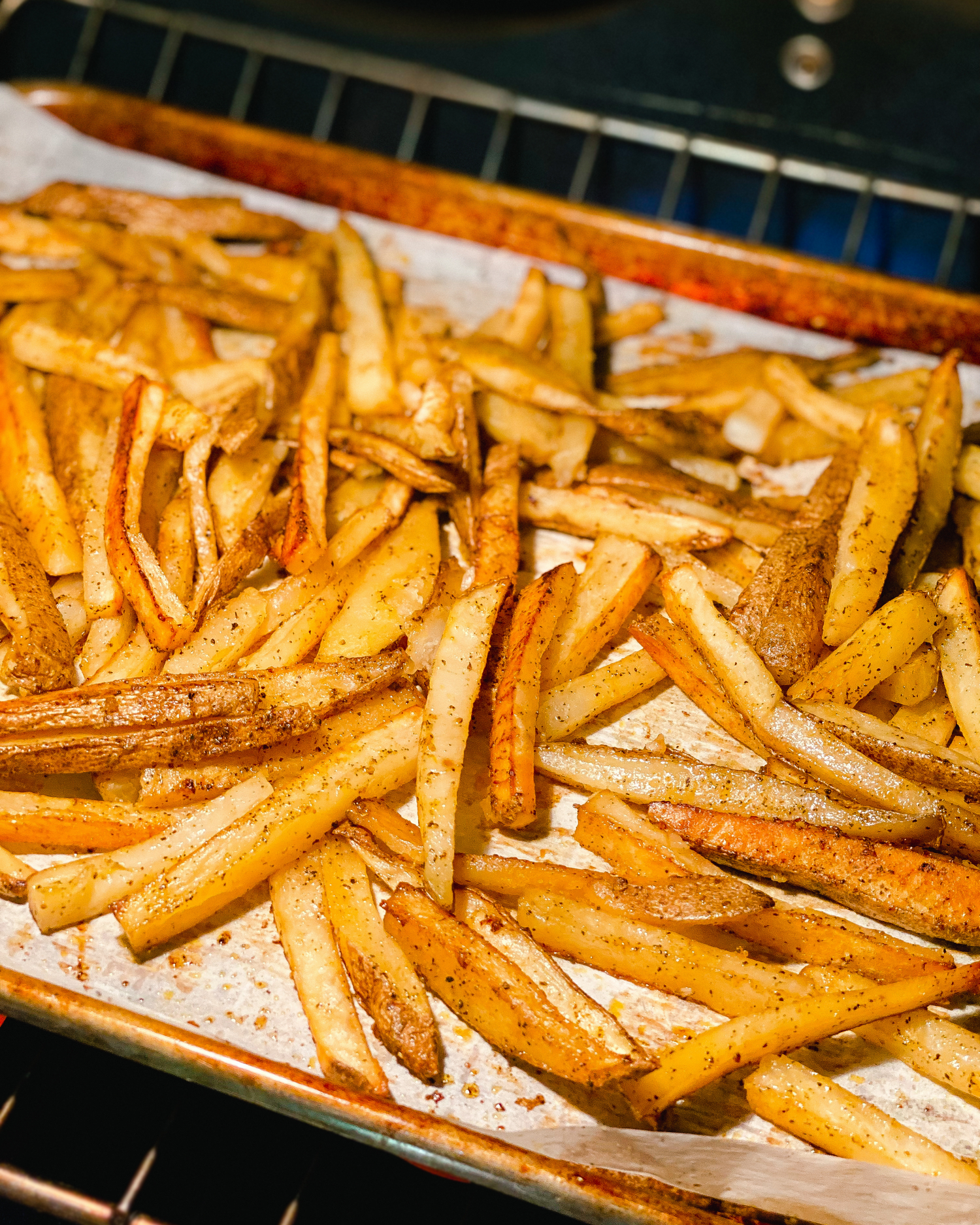 Freshly baked french fries on a parchment-lined baking sheet with visible seasonings.