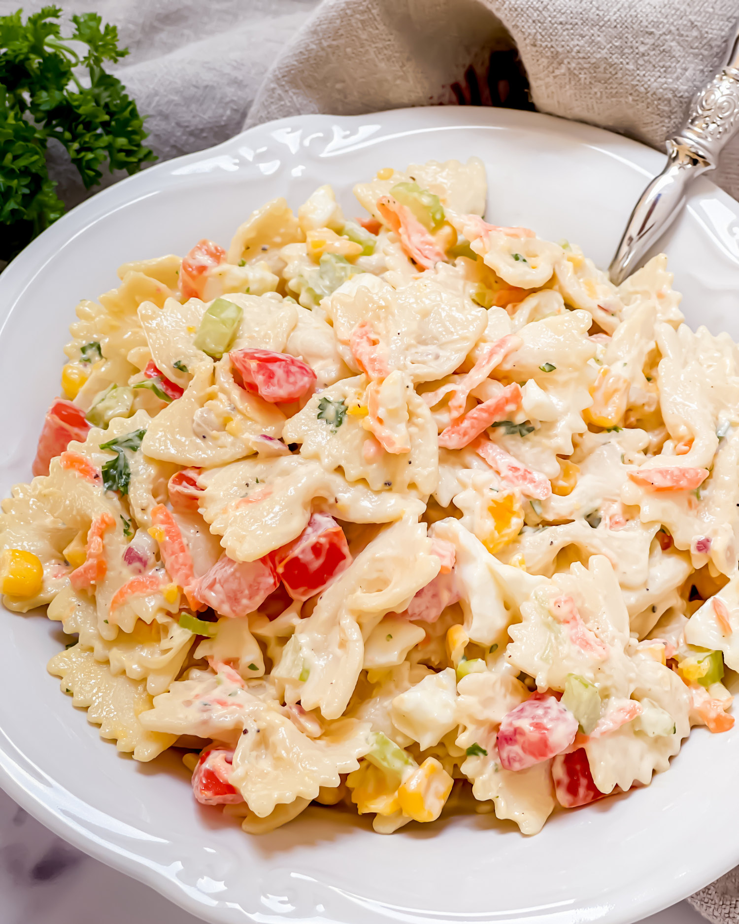 Fresh farfalle pasta salad with diced tomatoes, corn and creamy dressing on white dish.