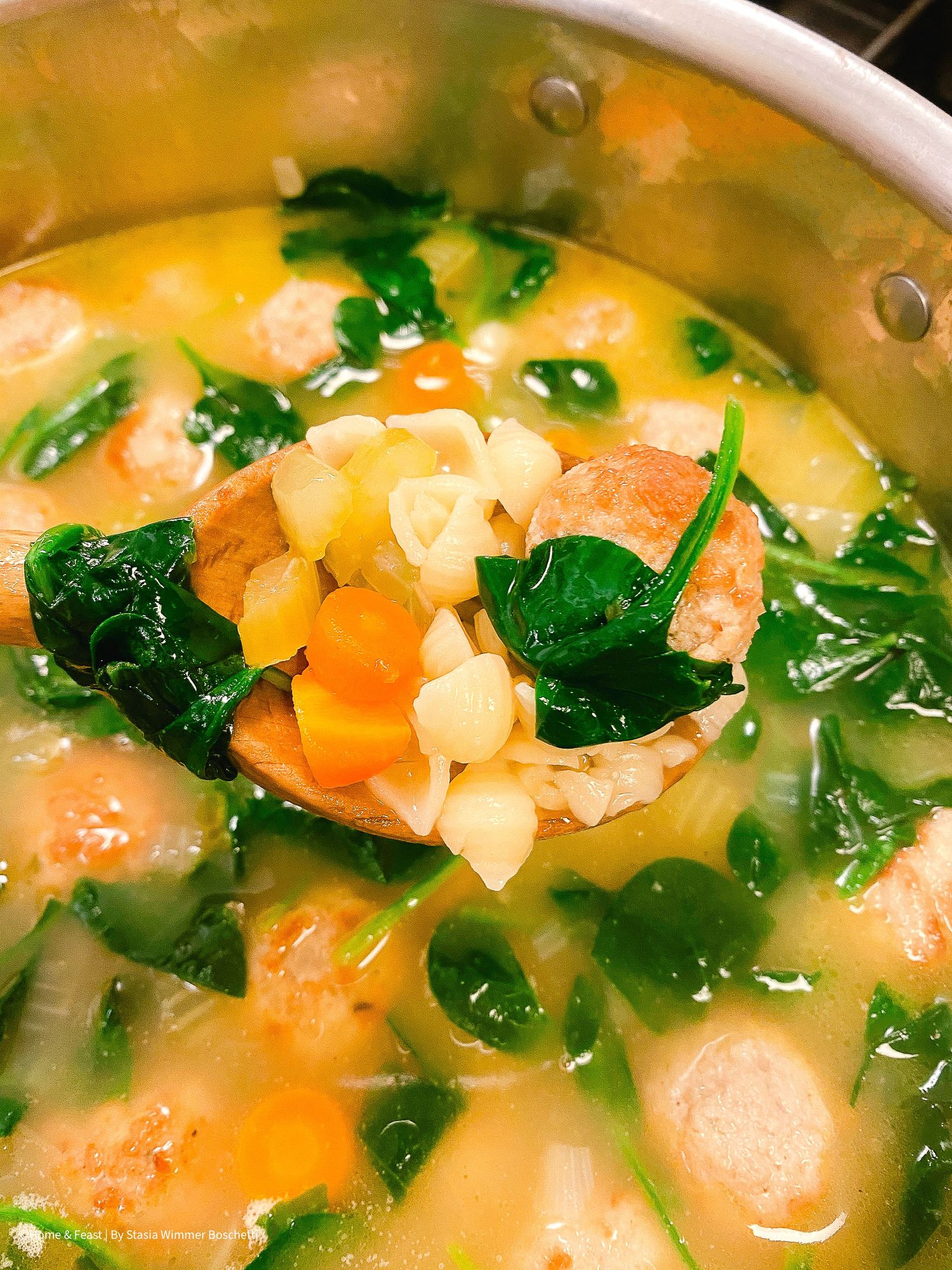 Close-up of Italian wedding soup showing tender meatballs, carrots, and fresh spinach in clear broth.