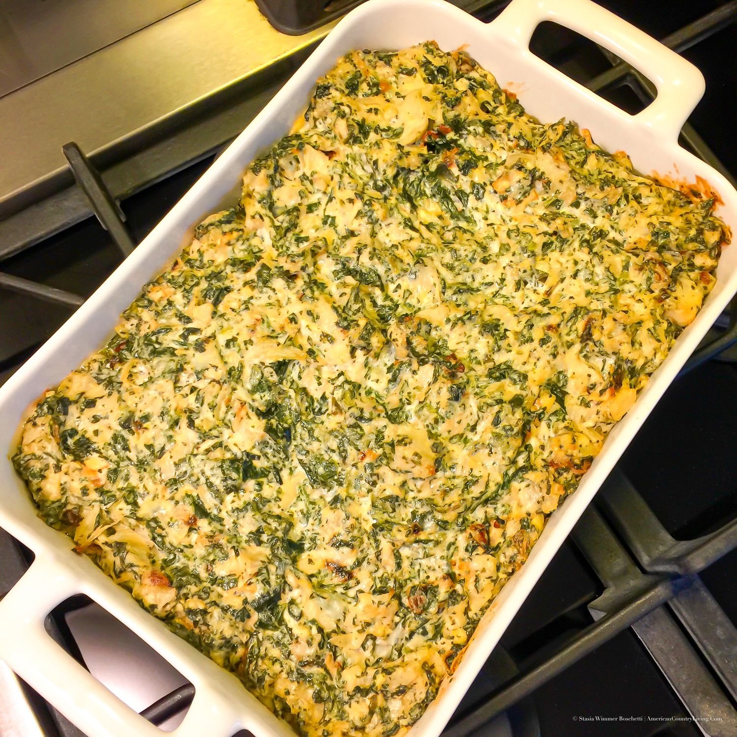 Golden baked spinach and cheese casserole in a white rectangular baking dish on a stovetop.