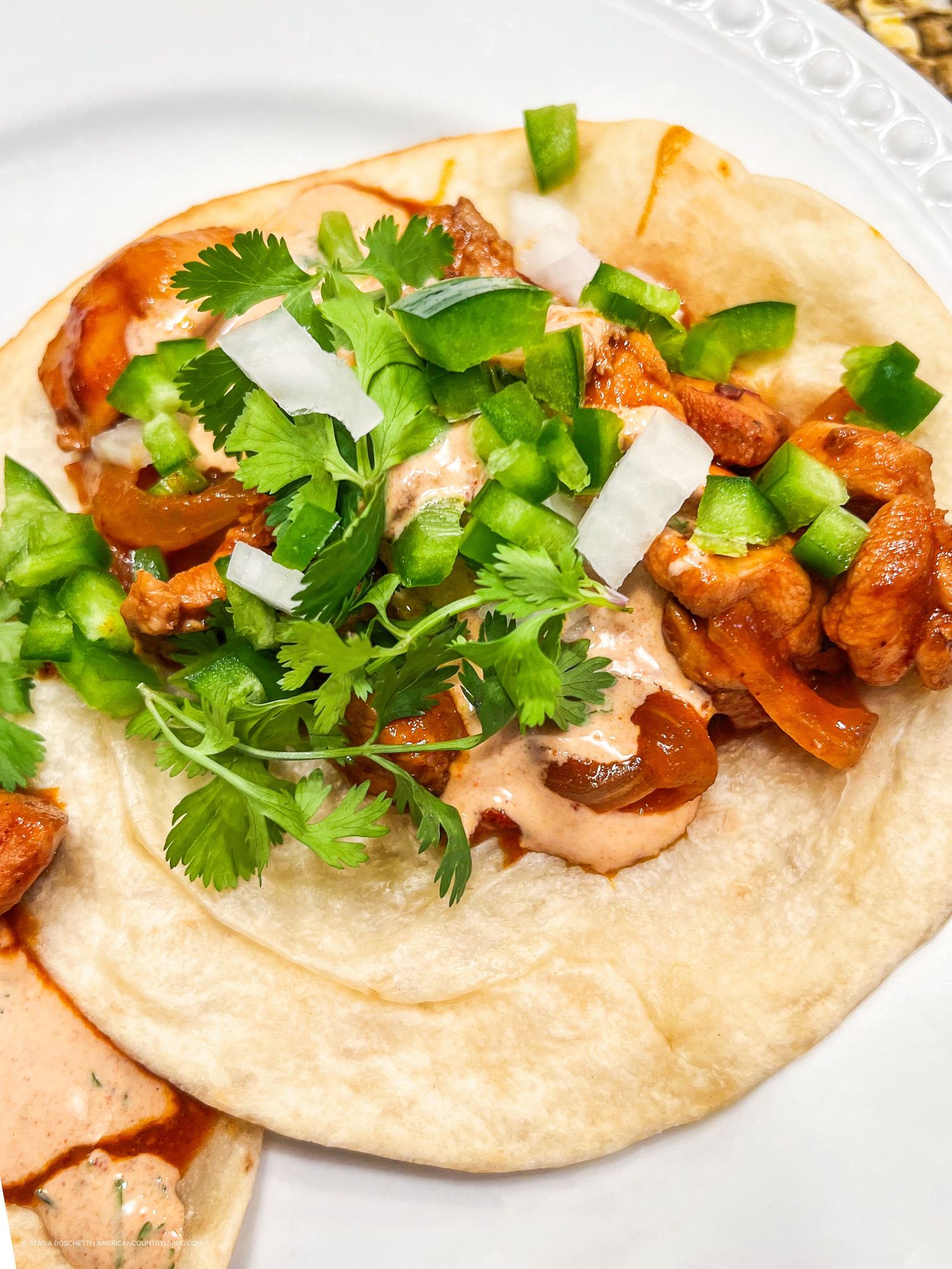 A flour tortilla topped with seasoned chicken, diced jalapeños, cilantro, and creamy chipotle sauce on a white plate.