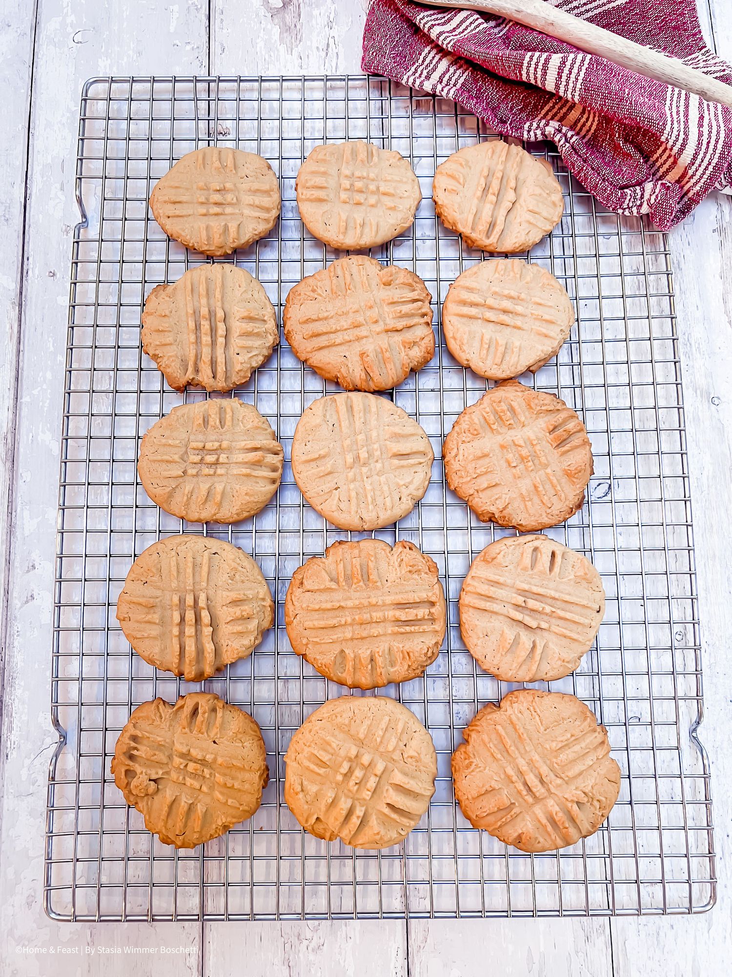 Freshly baked peanut butter cookies with crosshatch pattern cooling on a wire rack on a white wooden surface.