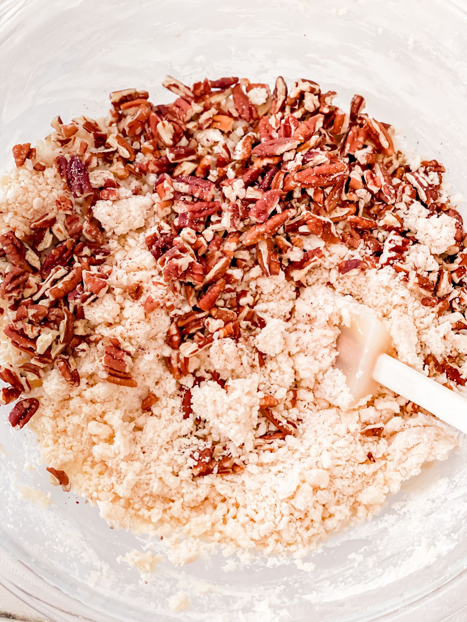 Chopped pecans mixed with flour and other dry ingredients in a white mixing bowl.