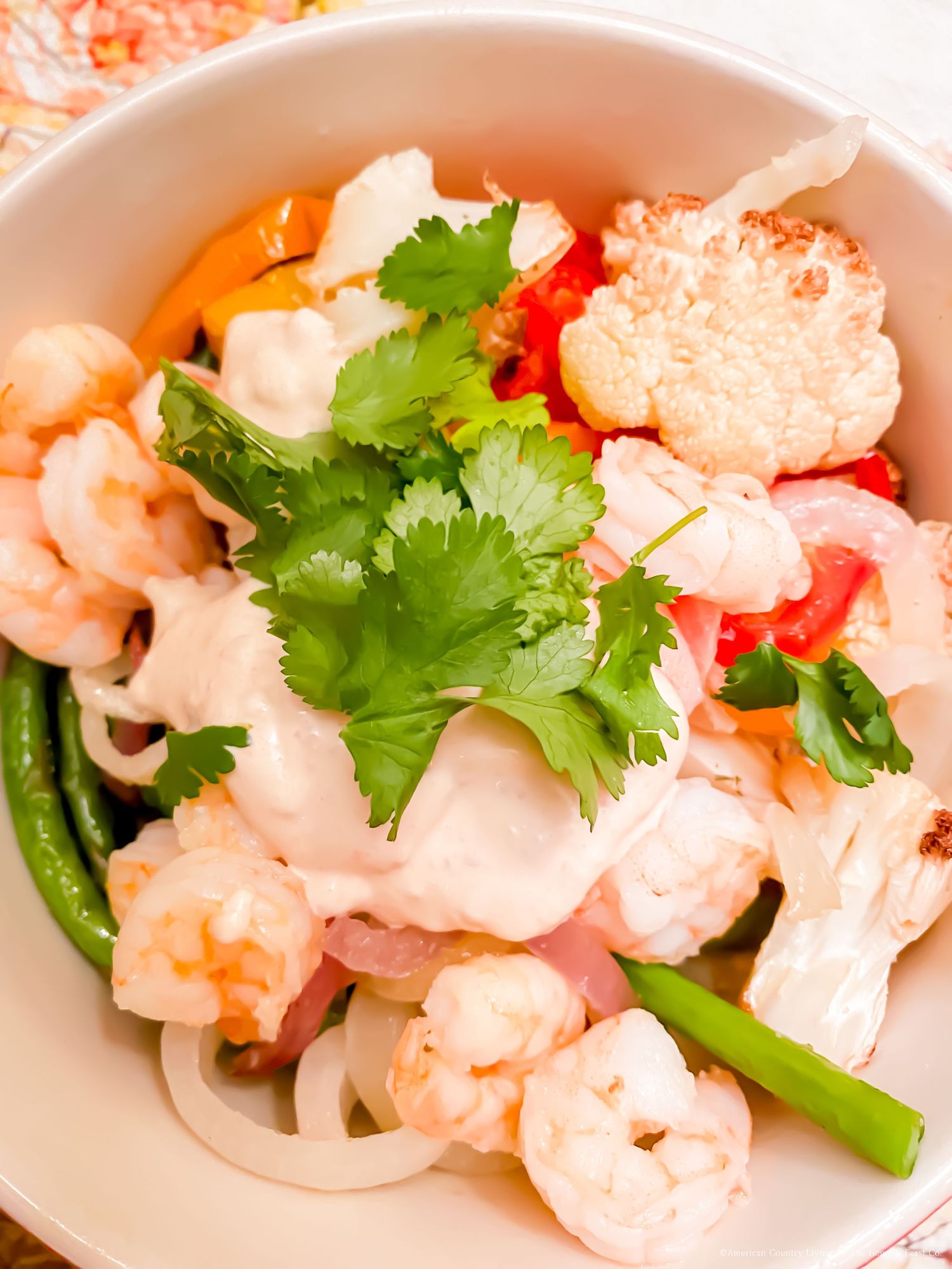 Fresh cauliflower salad with red peppers and cilantro garnish in a white bowl.
