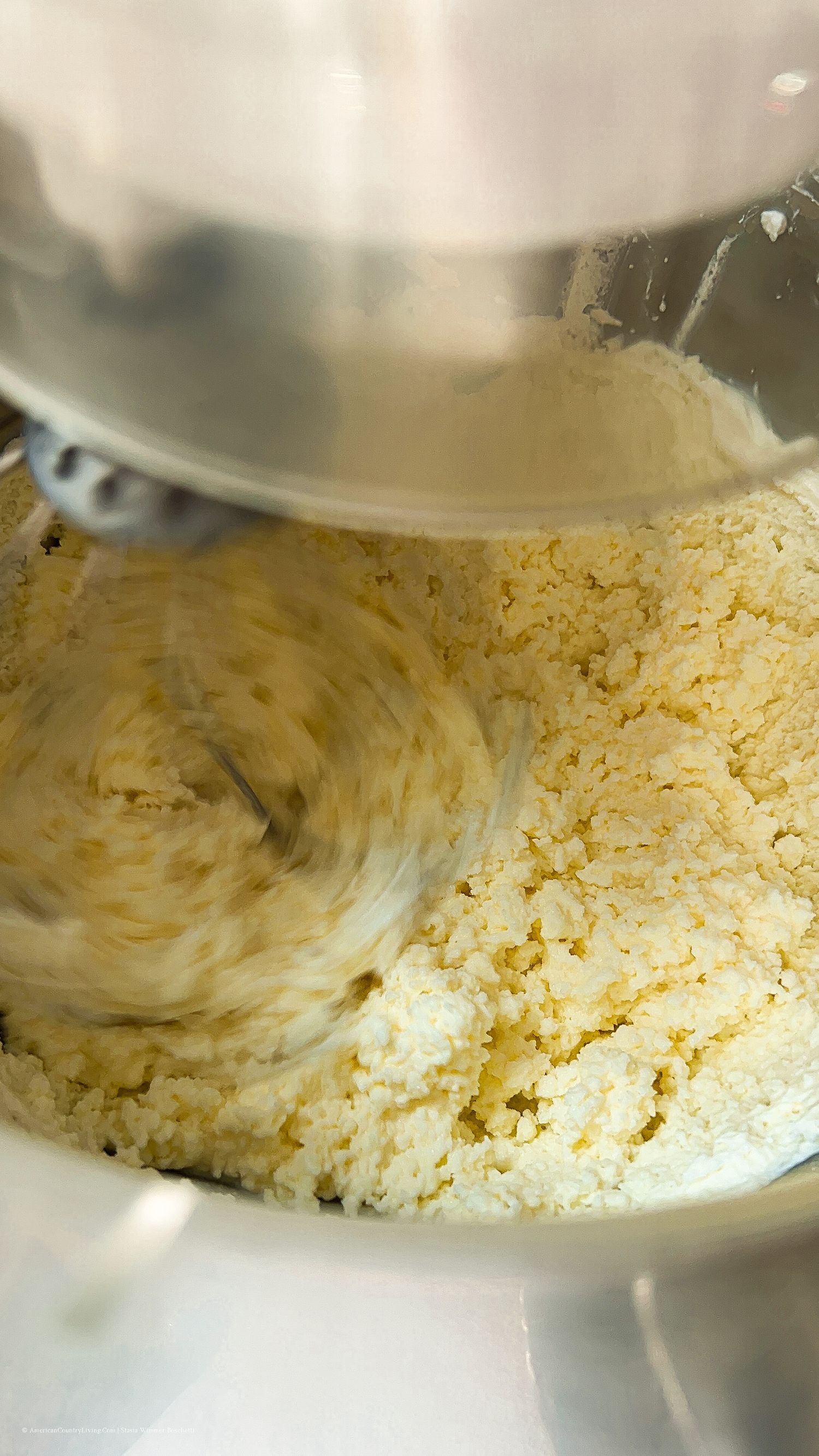 Yellow butter mixture being creamed in a stand mixer bowl showing smooth texture.