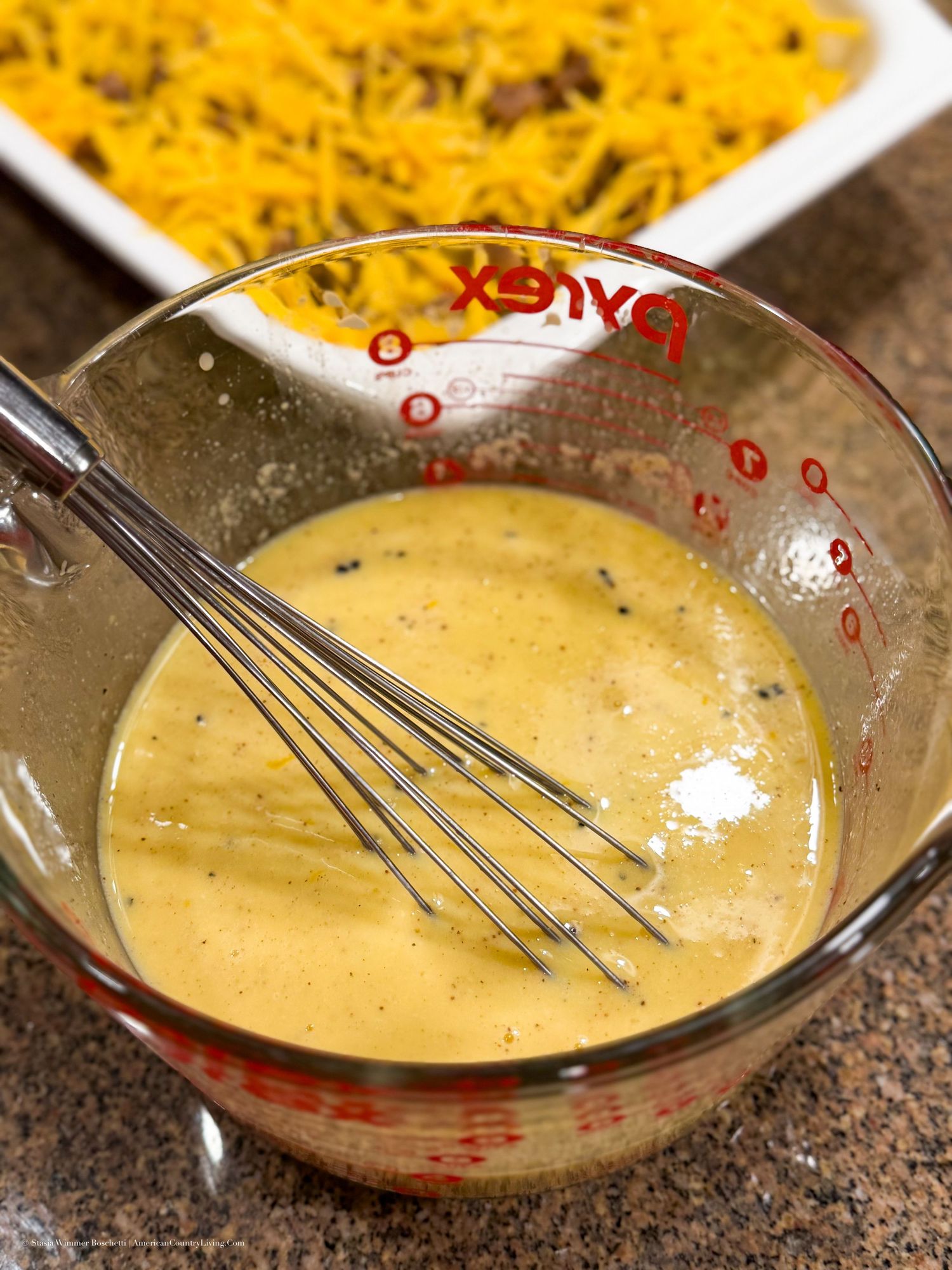 Pyrex measuring cup with whisked egg mixture beside a casserole dish with cheese and meat filling.